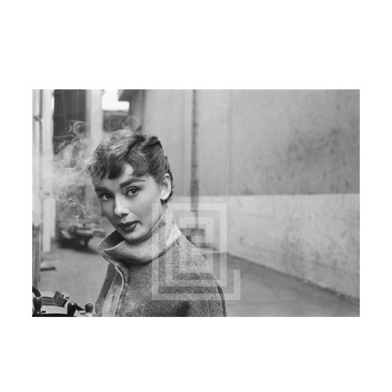 Mark Shaw Black and White Photograph – Audrey Hepburn in grauem Rollkragenpullover, leuchtend links mit Rauch, 1953