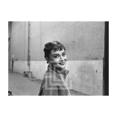 Audrey Hepburn con jersey gris de cuello alto, mira hacia la derecha sonriendo, con la cabeza ladeada