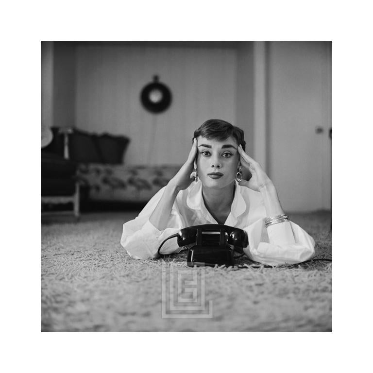 Mark Shaw Portrait Photograph – Audrey Hepburn in weißer Bluse mit Telefon, liegend, Finger auf Tempeln, 1953