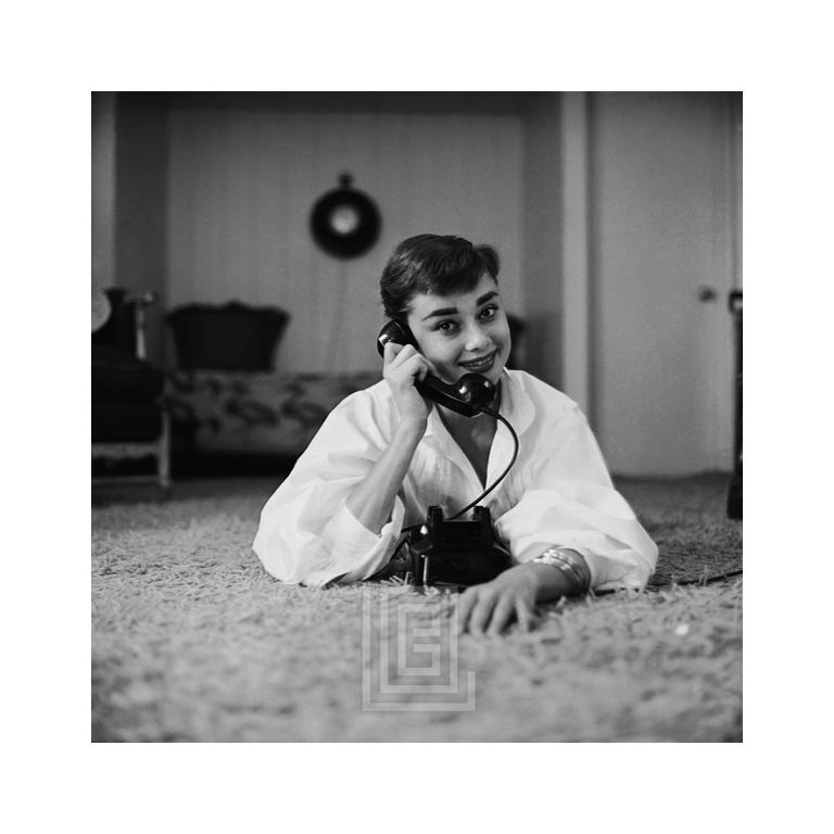 Audrey Hepburn en chemisier blanc avec téléphone, allongée, main sur le dessous, souriant