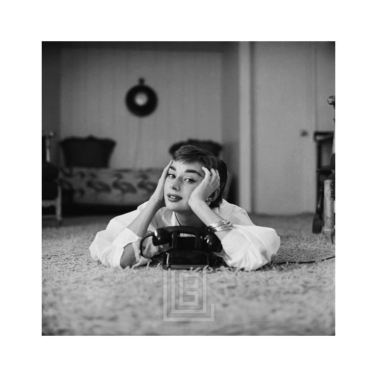 Mark Shaw Portrait Photograph – Audrey Hepburn in weißer Bluse mit Telefon, liegend, mit Händen im Gesicht, 1953