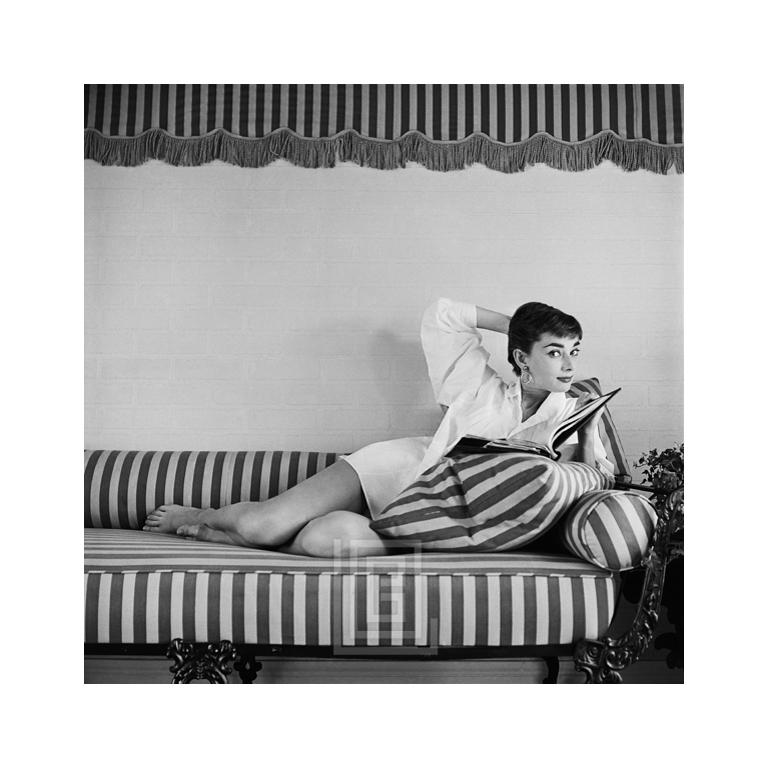 Portrait Photograph Mark Shaw - Audrey Hepburn sur canapé rayé, dossier en forme d'accoudoir, glances à droite, 1954
