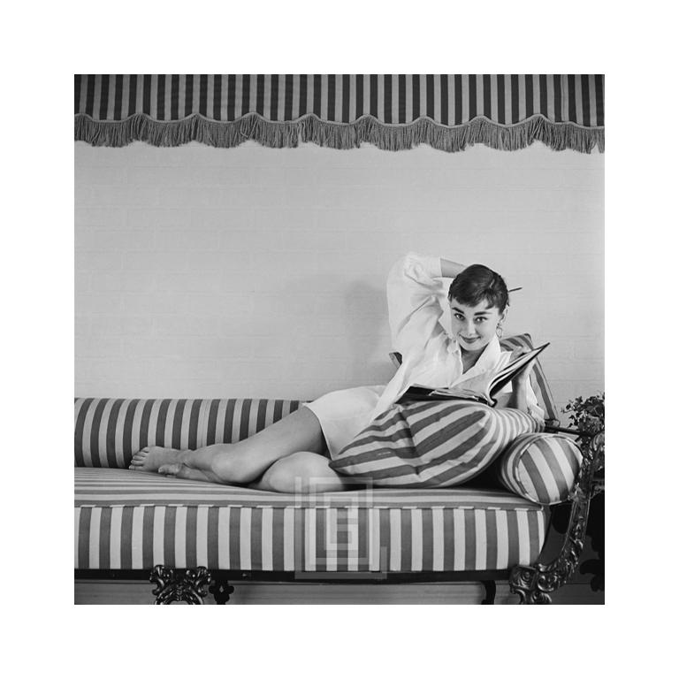 Black and White Photograph Mark Shaw - Audrey Hepburn sur canapé rayé, dossier à accoudoirs, souriant, 1954