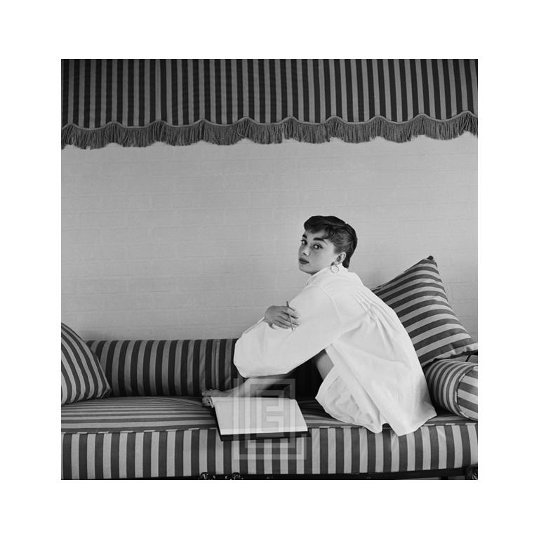 Portrait Photograph Mark Shaw - Audrey Hepburn sur canapé rayé, Hugs Knees, 1954