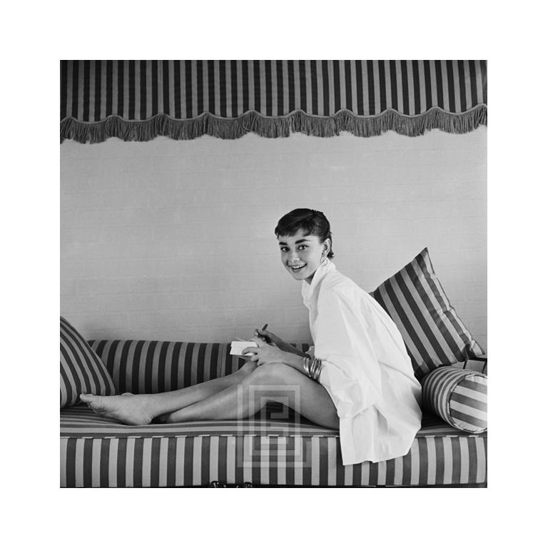 Portrait Photograph Mark Shaw - Audrey Hepburn sur canapé rayé, soufflant vers l'avant vers l'arrière, 1954