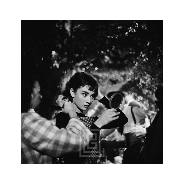 Black and White Photograph di Mark Shaw - Audrey Hepburn sotto un albero si ritocca il trucco, 1953