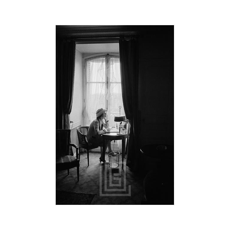 Mark Shaw Figurative Photograph - Coco Chanel Writes at Desk in Window, Head Up, 1957