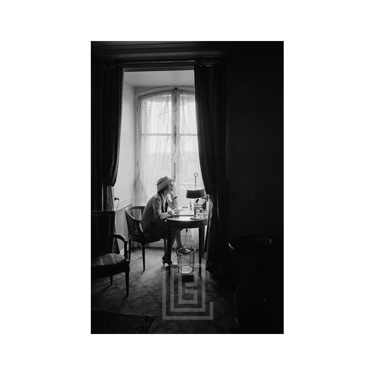Figurative Photograph di Mark Shaw - Coco Chanel scrive alla scrivania della finestra, a testa in su, 1957