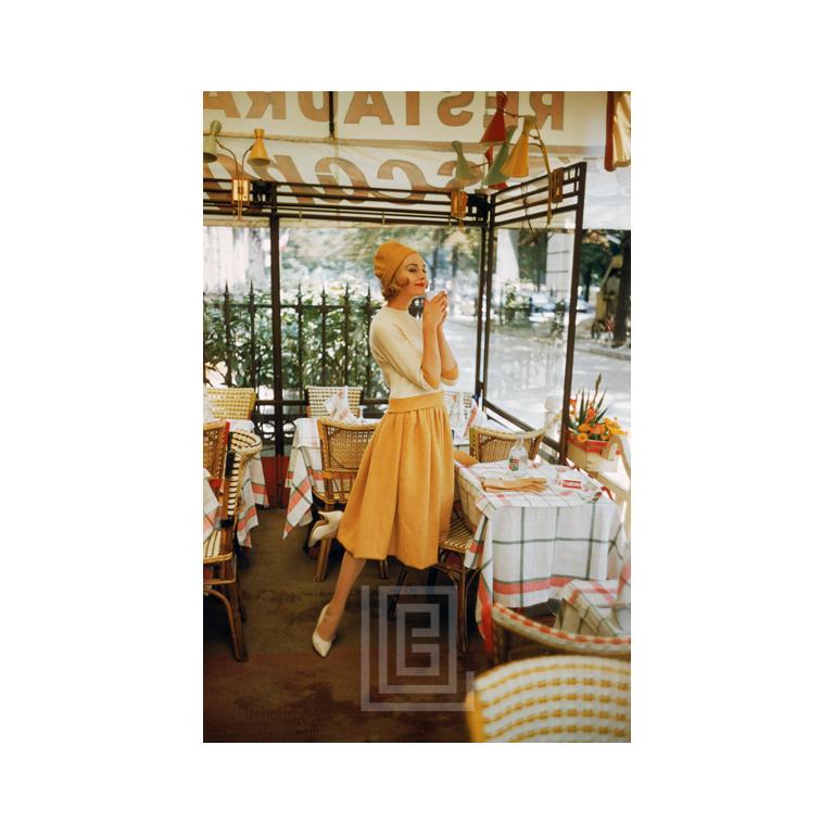 Figurative Photograph de Mark Shaw - Modelo vestida de amarillo en un café de París, 1957