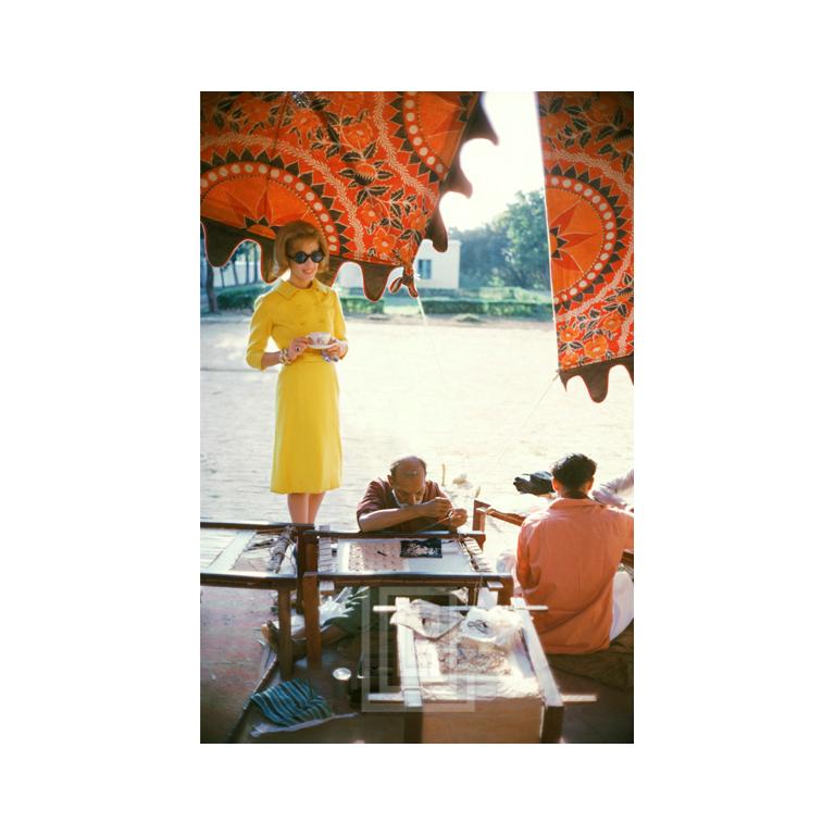 Mark Shaw Color Photograph - Tiger Morse in Yellow Suit Watches Sewing, 1962