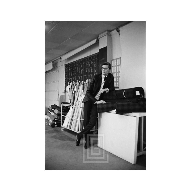 Mark Shaw Portrait Photograph - Yves St. Laurent Leans on Bolts of Fabric, 1960