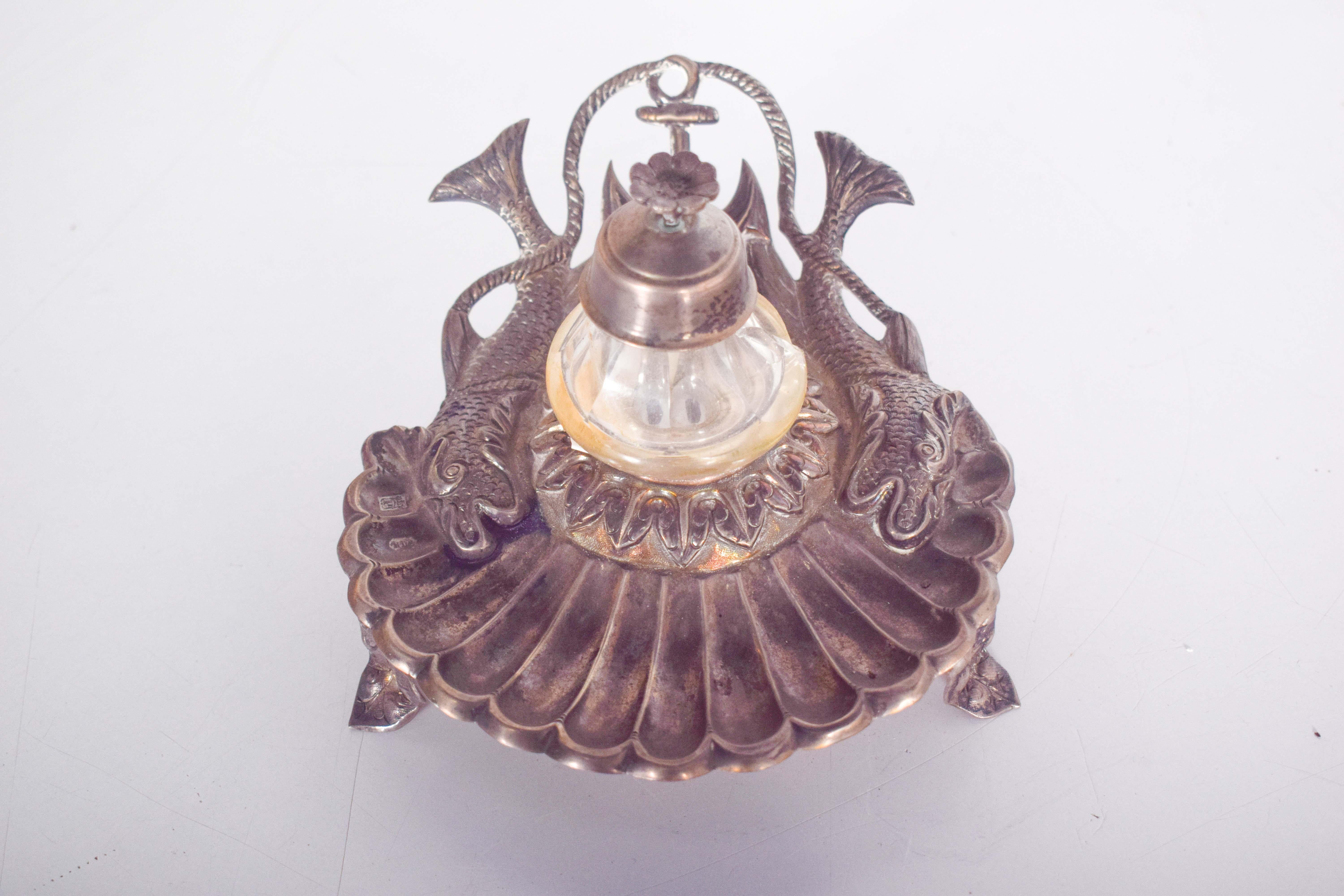 Un calamaio in argento marcato e splendidamente realizzato a forma di conchiglia, con serbatoio dell'inchiostro in vetro per un tocco classico. Il calamaio è intricatamente decorato con motivi che evocano il mare, tra cui una conchiglia, un'ancora,