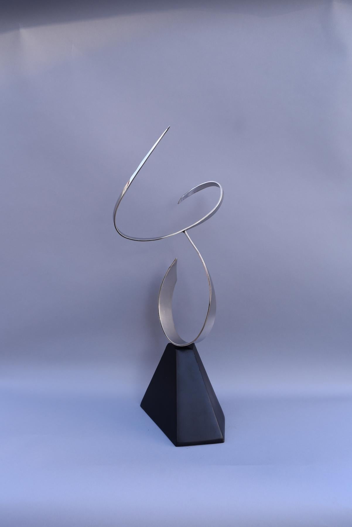 Dans cette sculpture en acier inoxydable de Marko Kratohvil, les courbes gracieuses de deux segments d'acier lisse se rencontrent en mouvement, créant une forme figurative abstraite. Cette sculpture de table est posée en équilibre sur une base en