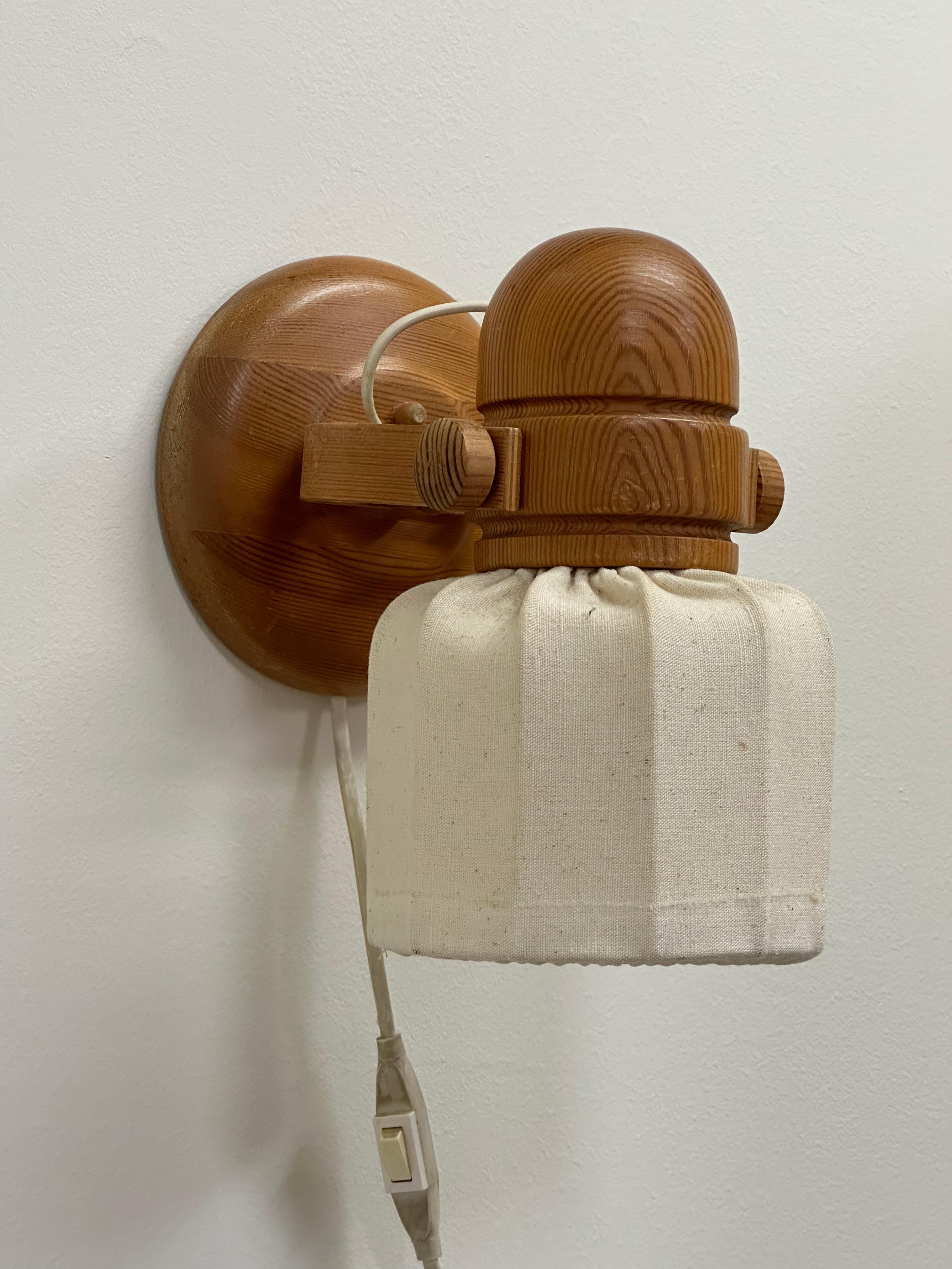Simpatica applique vintage prodotta da Markslöjd in Svezia intorno agli anni Settanta. La struttura in legno di pino e il paralume in tessuto danno una sensazione di organicità davvero piacevole. Funziona bene e si può regolare un po'