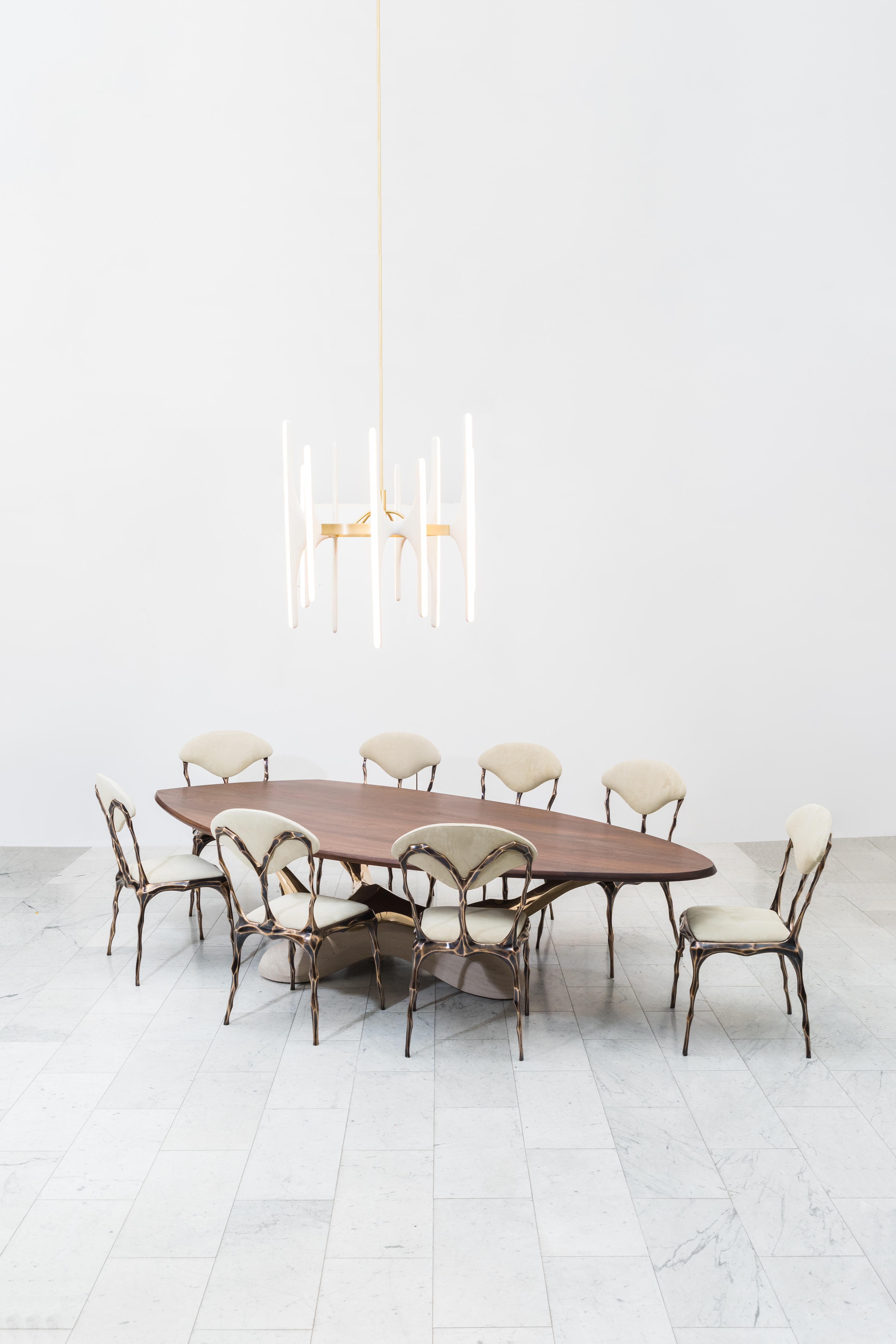 Markus Haase’s one-of-a-kind 12-foot handcrafted dining table features a sculpted American black walnut top resting on a bronze tripod, supported by a carved limestone base. The organically shaped bronze tripod is sculpted in foam and then cast in