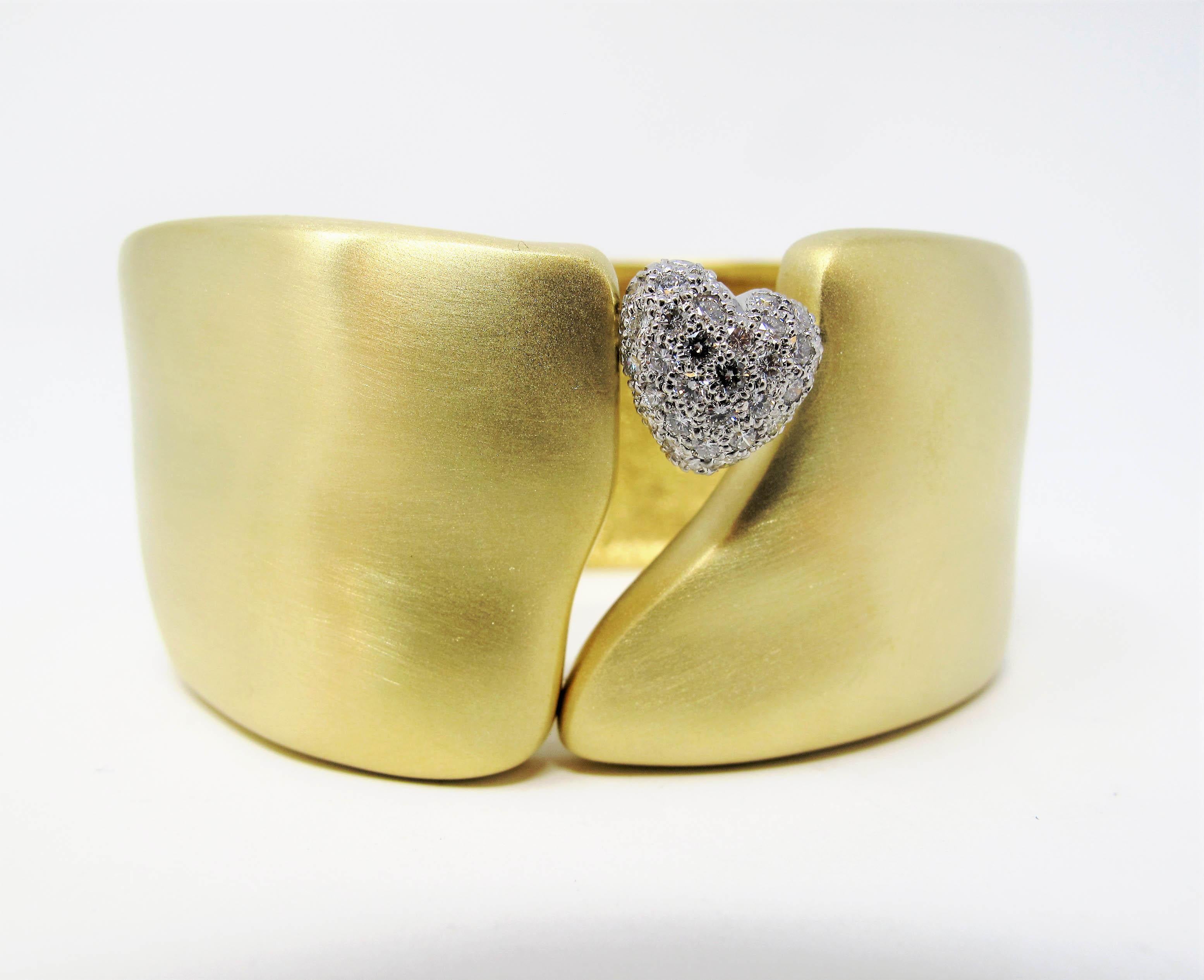 This bold, contemporary statement piece fills the wrist with understated sophistication. The incredible cuff bracelet has a subtle hammered design in a brushed gold finish, accented by a single glittering pave diamond heart. The sleek, modern design