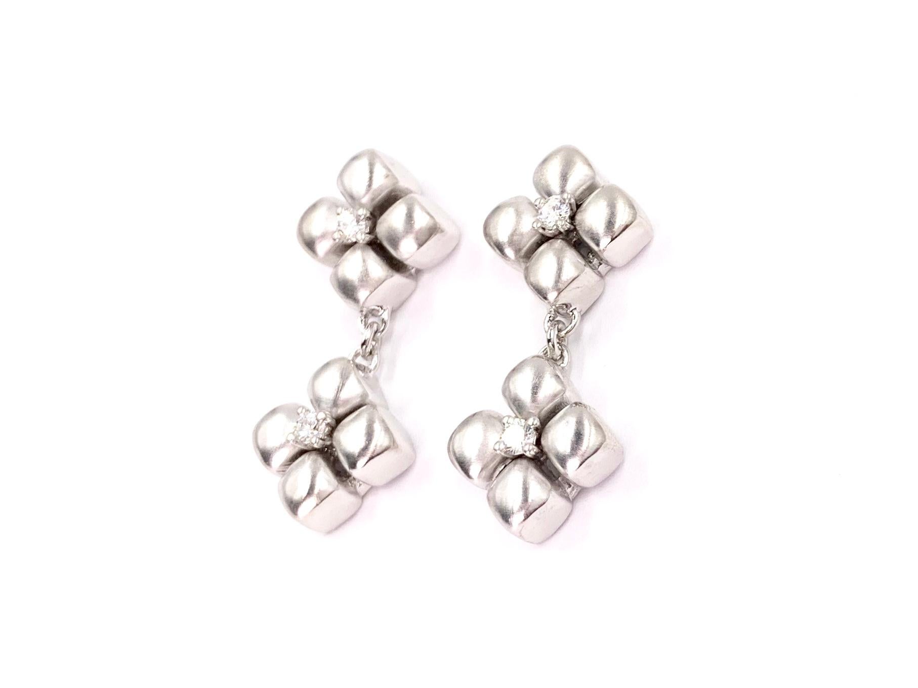 Made with superior quality by Marlene Stowe. These timeless and chic floral drop earrings are made of platinum and 18 karat white gold with a round brilliant diamond set in the center of each flower for a subtle sparkle. Earrings have a diamond