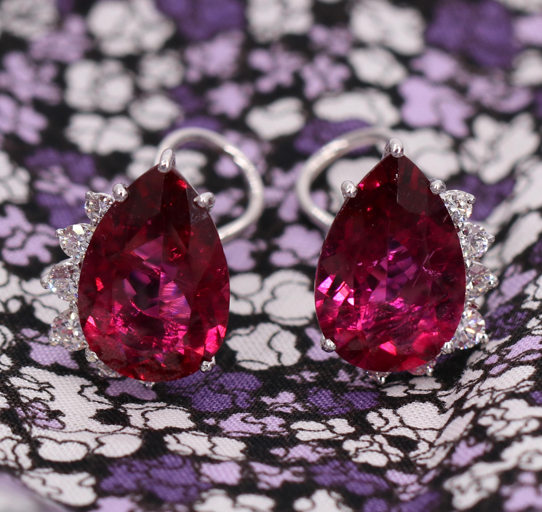 A pair of ladies 18K white gold earrings, each centered around a vivid pear-shaped rubellite tourmaline measuring approximately 24mm X 27mm. The tourmaline are a balanced and saturated red with a slight purple overtone. Swooping around the base of
