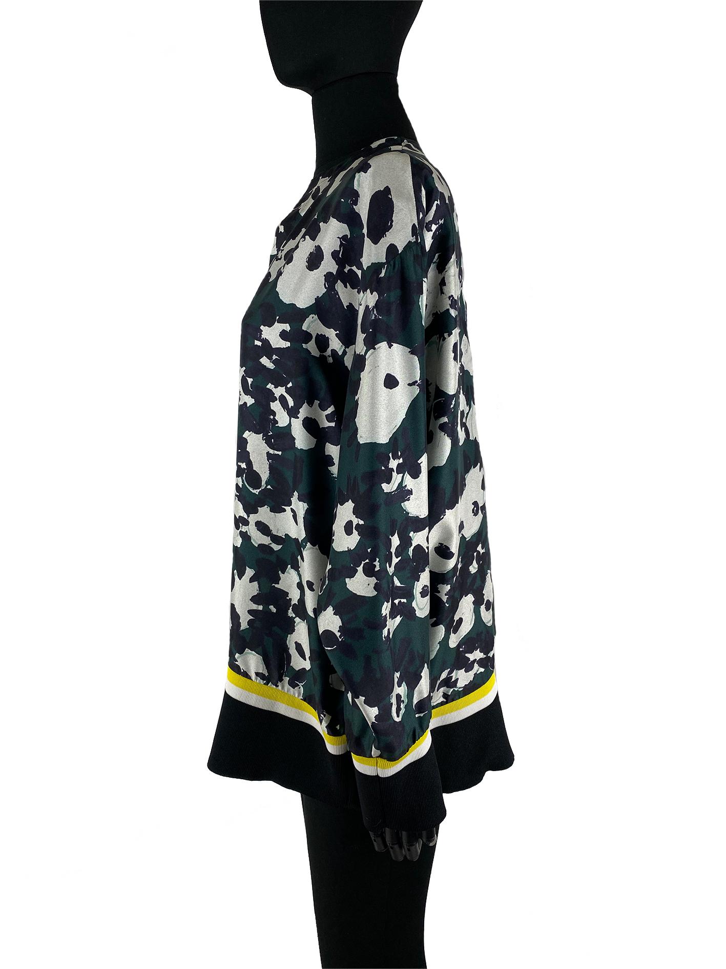 A camo print Marni top with shades of forest green, white and black. The top features an elasticated waistband and cuffs with yellow, white and black around the length of them in horizontal stripes. The collar of the top goes into a sharp ‘V’. The