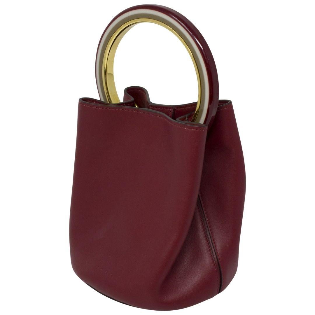 Okay we love her.. She's so posh! Crafted in cherry grained calfskin leather with the cutest round resin handle in metal in a complementary multicolor, there is also a removable strap and a pouch for added versatility! The snap closure opens up to a