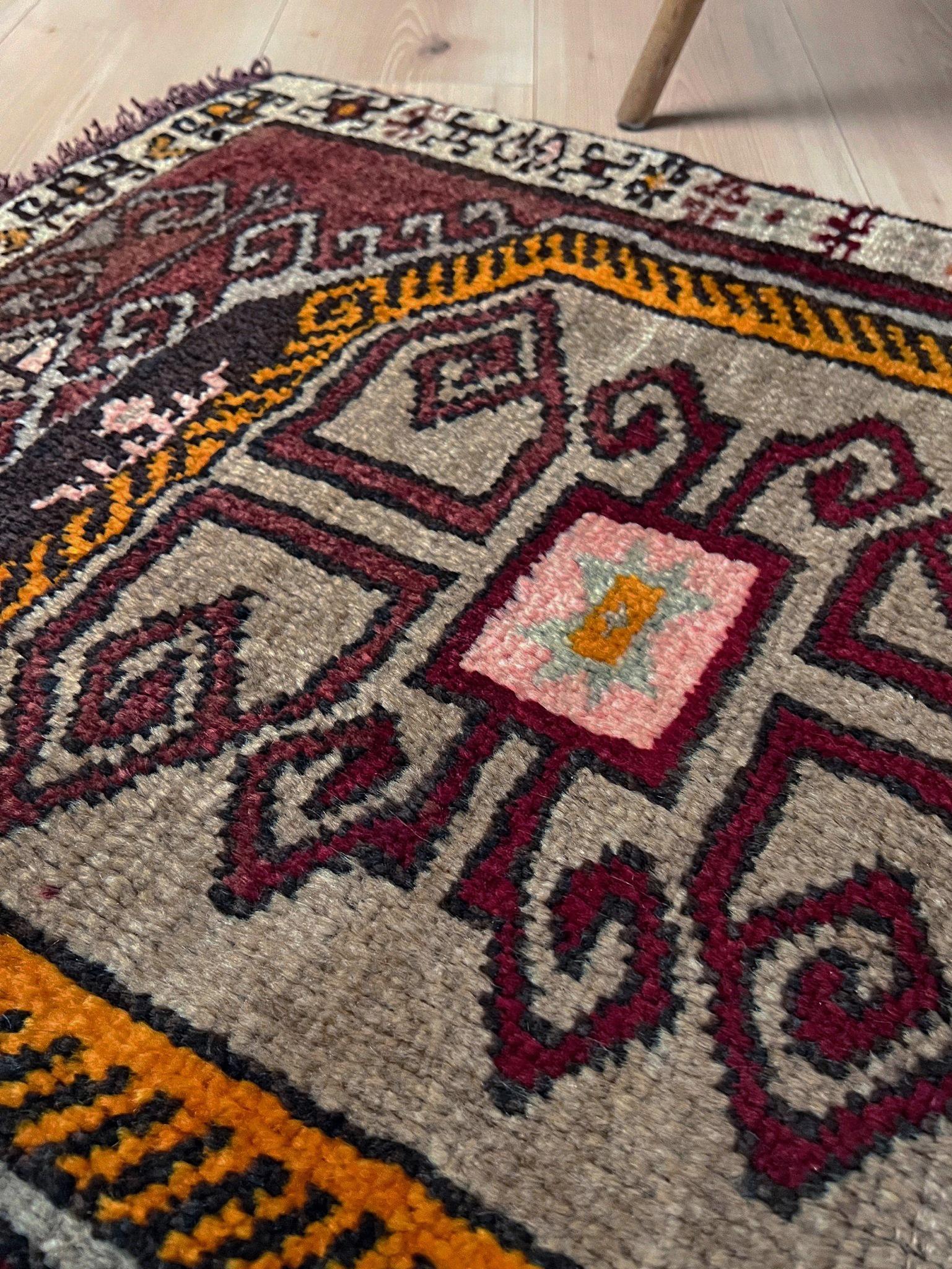 Un magnifique mini tapis turc vintage riche en caractère, tissé à la main avec de la laine douce et présentant un centre tribal audacieux encadré par des tons chauds et terreux. Son format compact  Sa taille en fait un objet idéal pour les entrées,