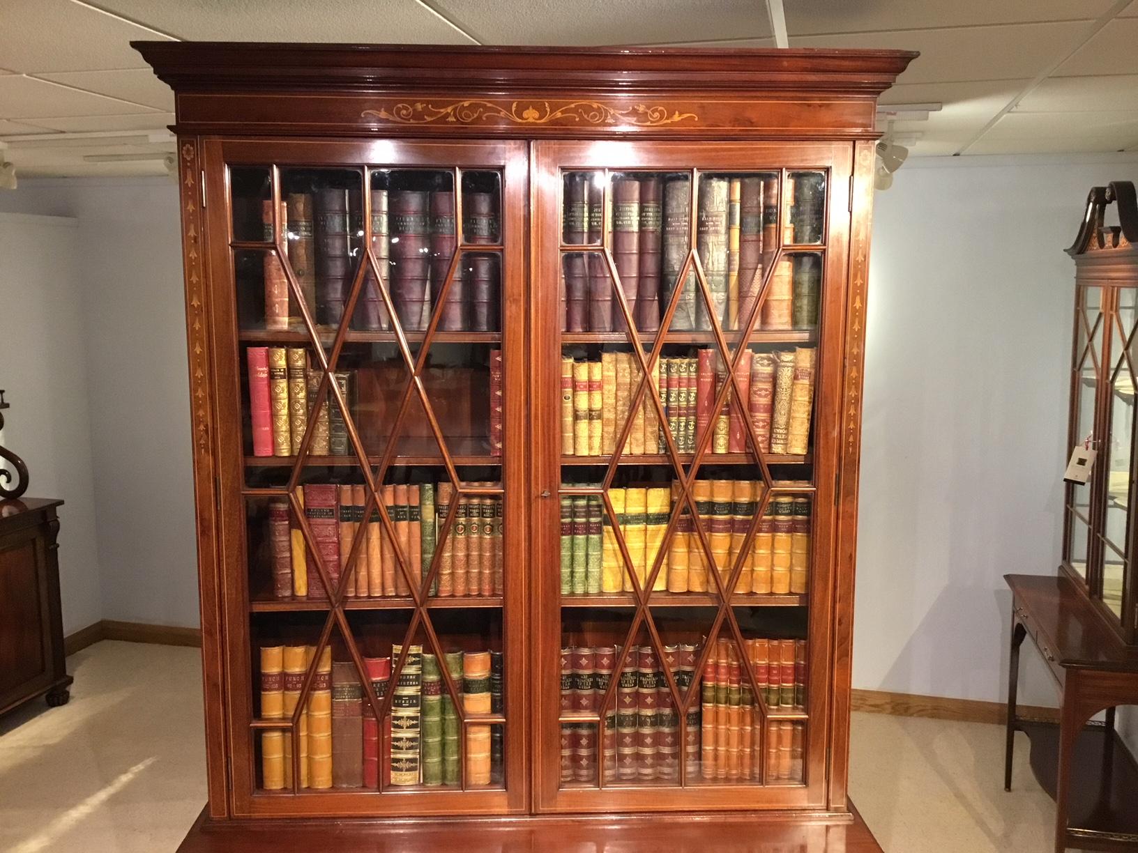 A Superb quality marquetry inlaid Edwardian Period antique bookcase. The upper section with a stepped and moulded cornice above a marquetry inlaid frieze and having twin astragal glazed doors, which open to reveal four adjustable mahogany shelves