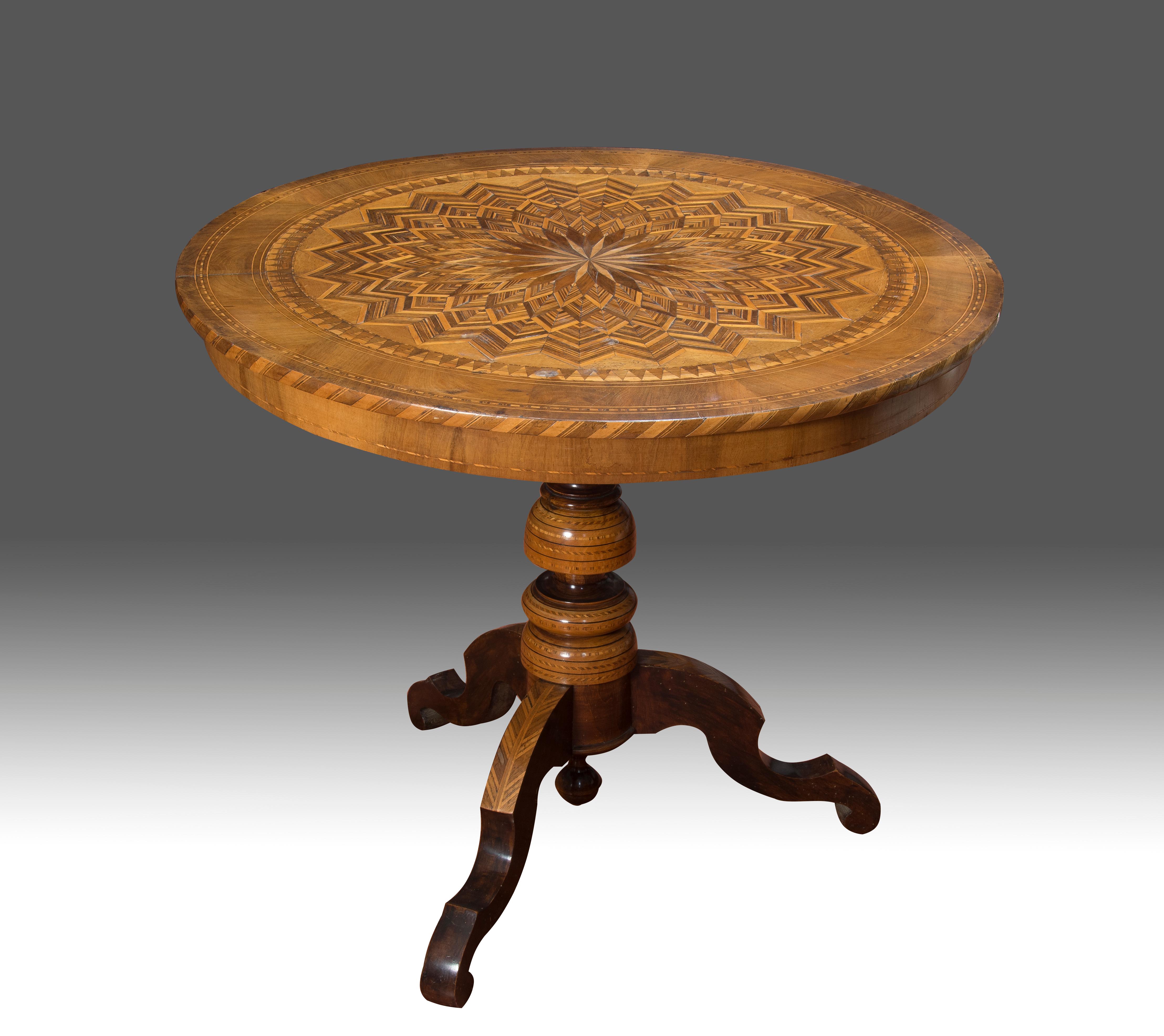 On three legs stands the table with turned leg, which supports the tabletop, round and with a magnificent geometric marquetry decoration, made by taking a simple element and repeating it in a circular sense, combined with bands of triangles and