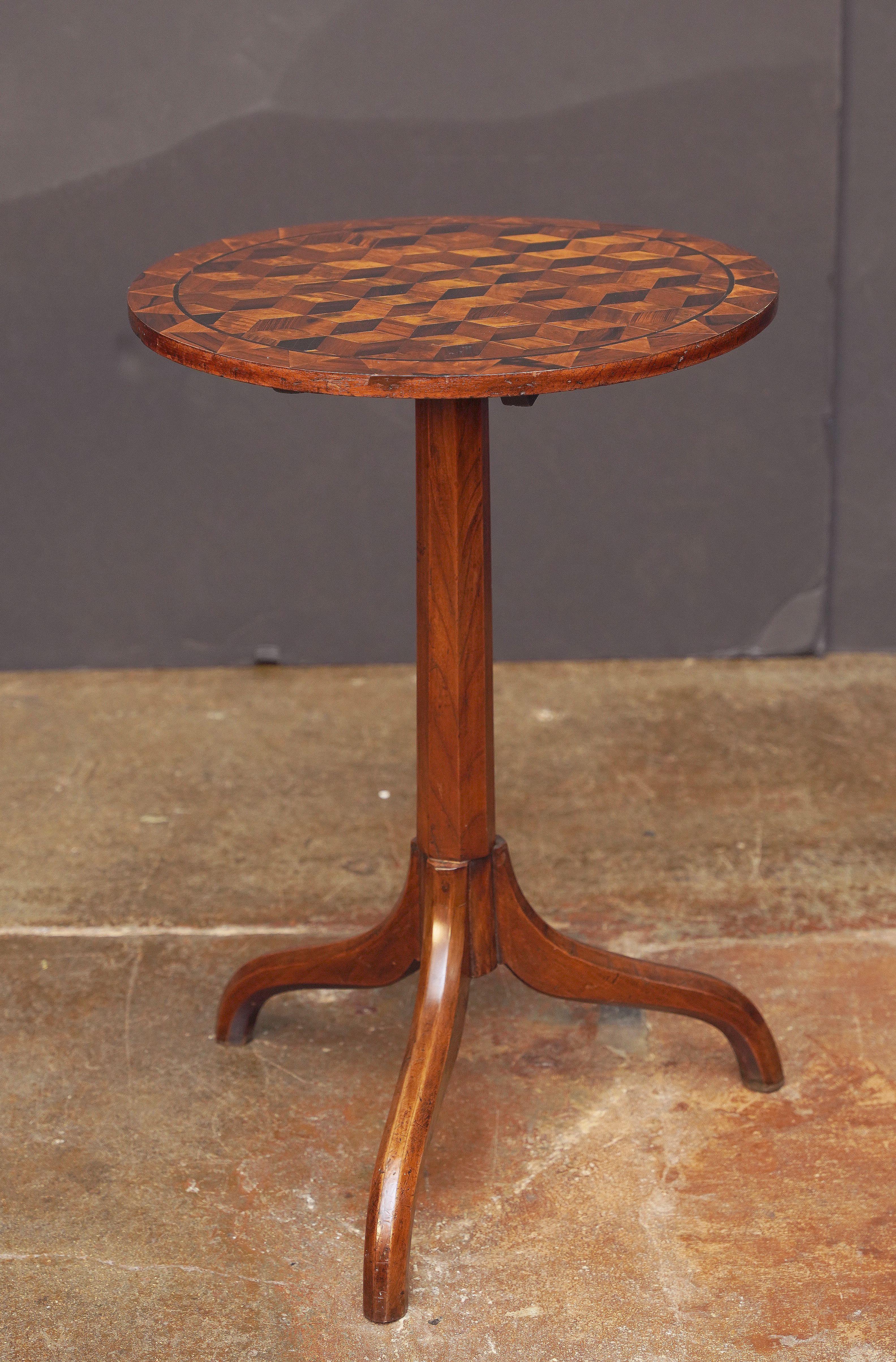 A fine English marquetry round tilt-top tripod table from the 19th century, featuring a circular wood top inlaid with a beautiful geometric design set upon a pedestal tripod base of patinated wood.

H 28.25 in x Diameter 19 in

Standing H 38.63 in