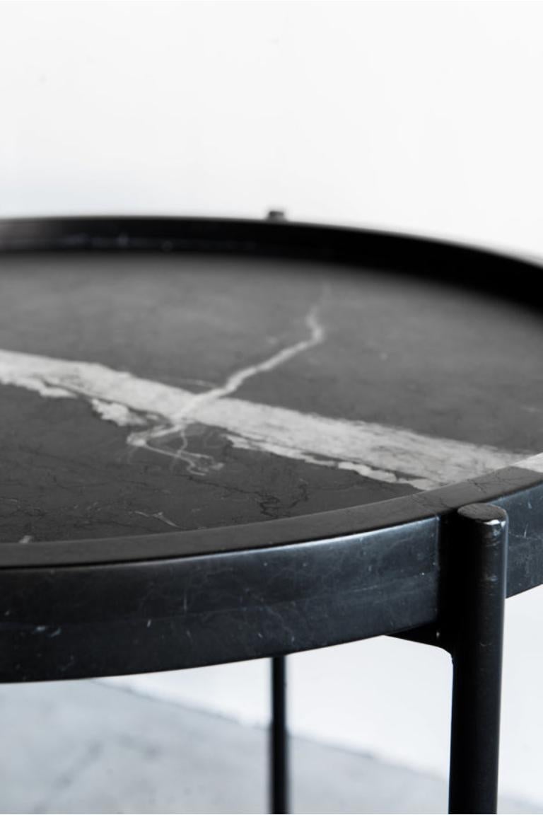 The Marquina Side Table is a sophisticated, minimalist accent piece. The honed Nero Marquina marble top features a stacked edge that creates a subtle rim, while the thin matte black base made of round stock steel adds an understated refinement to