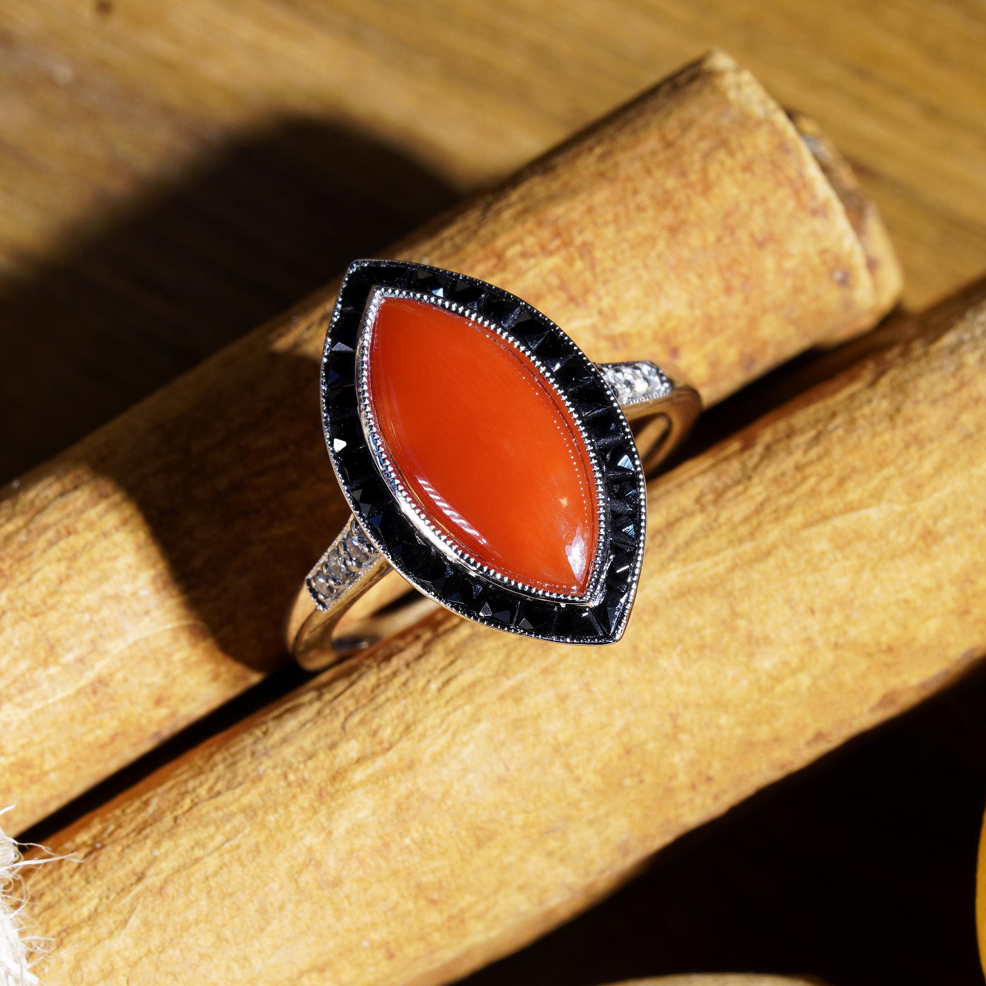 Art Deco Style marquise coral with onyx and diamonds ring in 14k white gold. Centered with an estimated 1.20 carat marquise shaped AKA coral in a milgrain setting, bordered by a row of French cut black onyx and flanked to either side with diamond