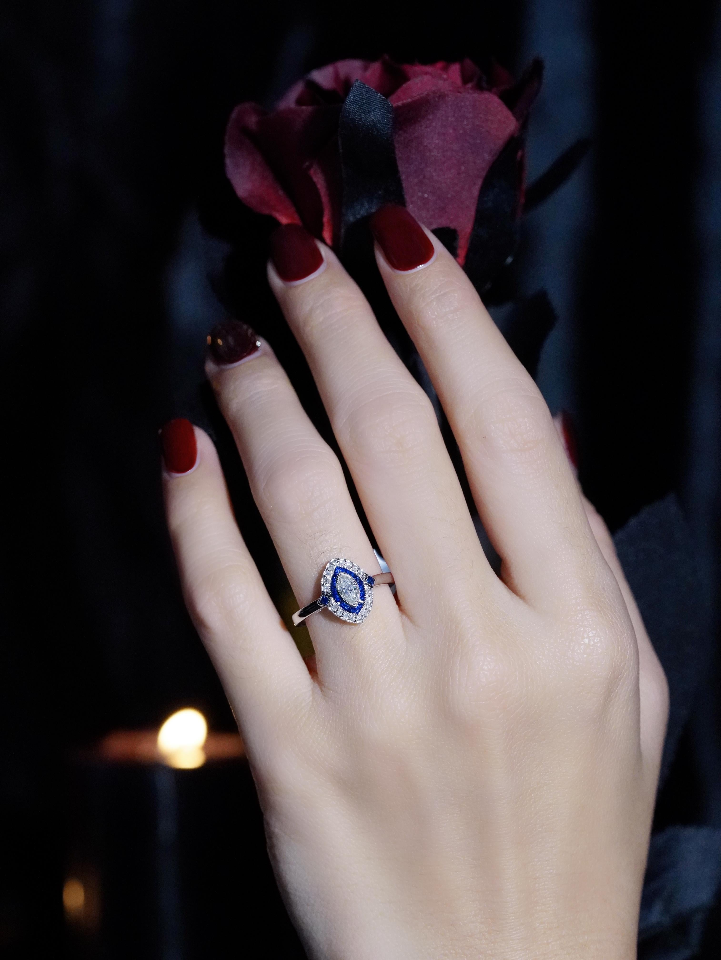 Un diamante marquise abbagliante è al centro della scena con una brillantezza accattivante. Circondato da un'aureola di ricchi zaffiri taglio francese, il design crea un contrasto straordinario che mette in risalto l'eleganza allungata del diamante.