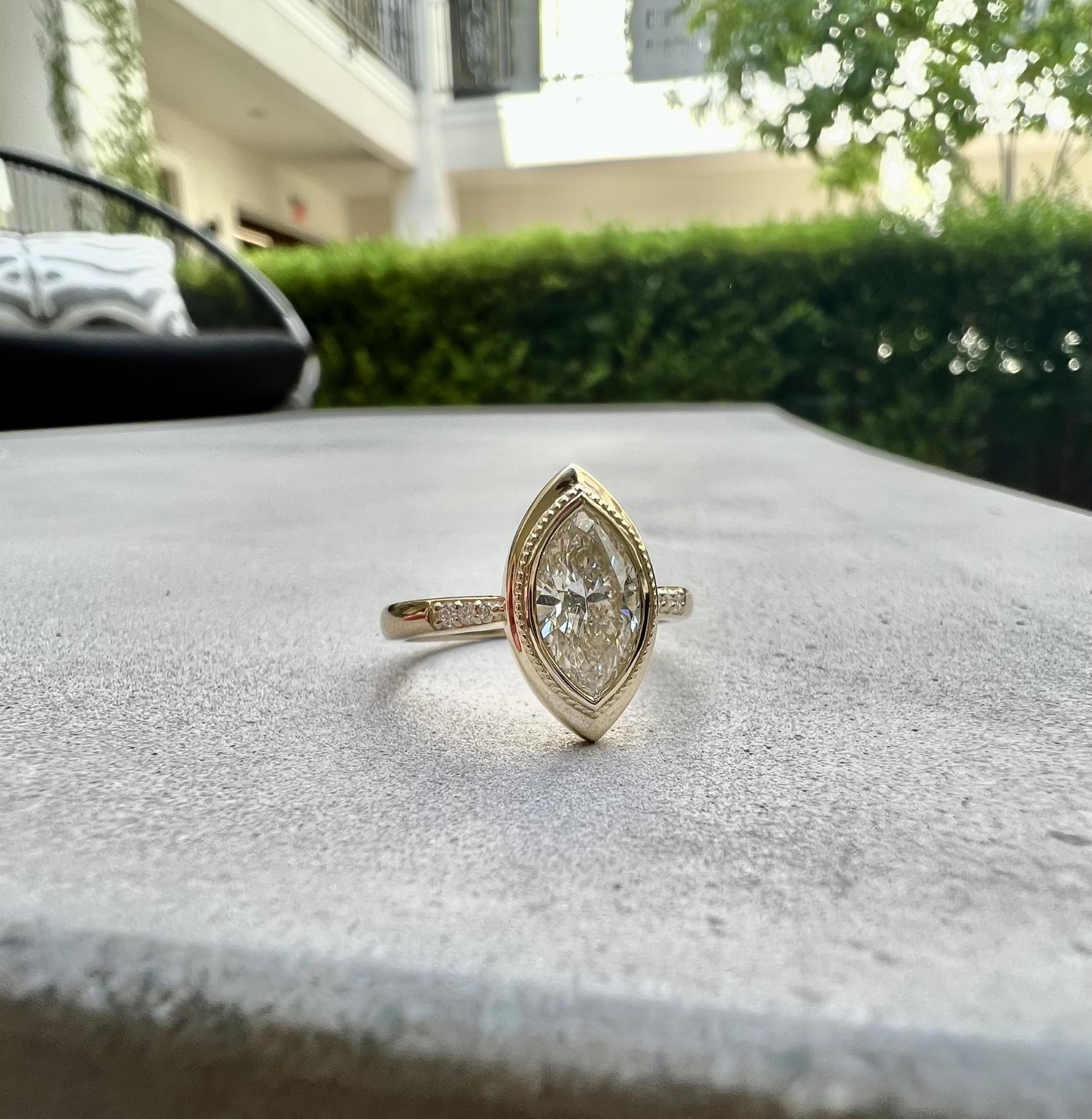 This exquisite diamond ring features a stunning marquise-cut diamond set in a beautiful bezel setting that showcases its elongated, elegant shape. This marquise diamond 1.21 carats and is K in color with SI2 clarity. The diamond is complemented by
