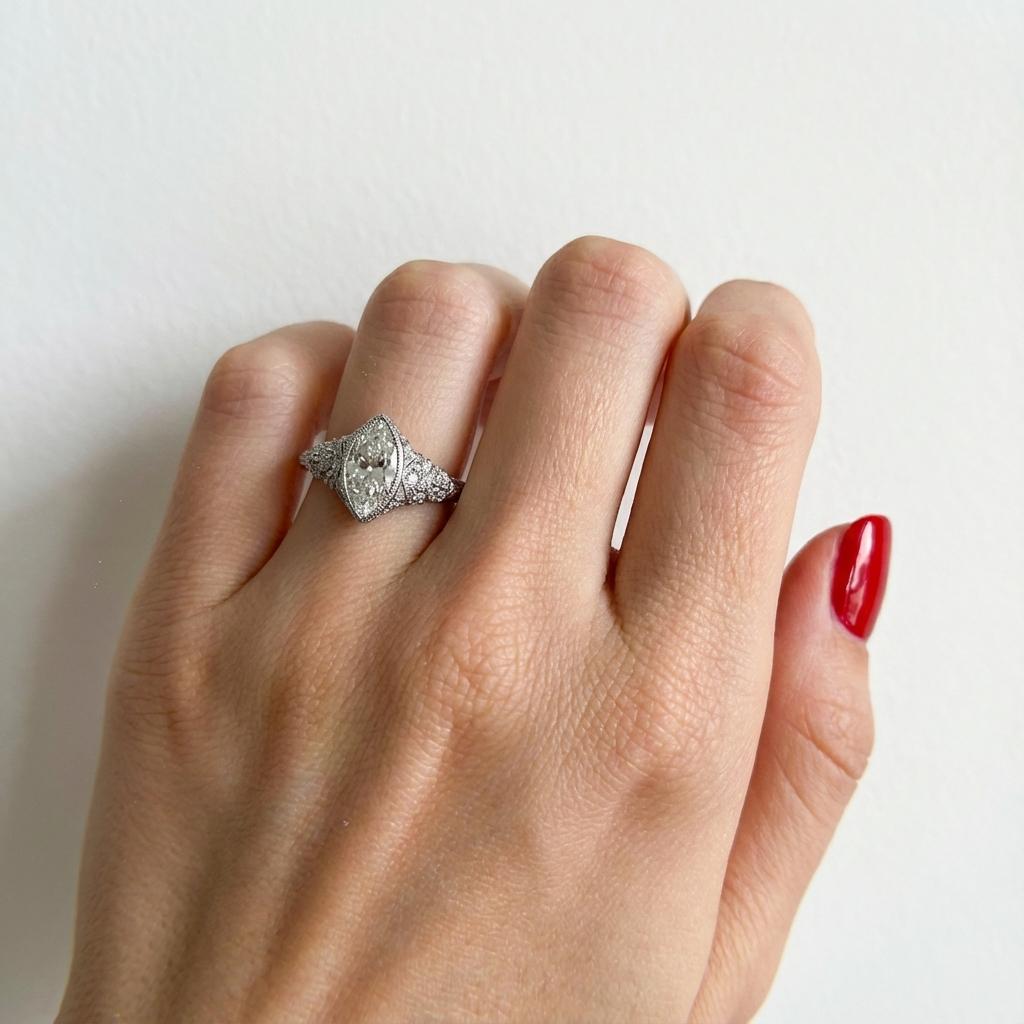 Ein Verlobungsring im Vintage-Stil aus 14 Karat Weißgold mit einem Diamanten im Marquiseschliff von ca. 0,69 Karat. 
Der Stein ist sicher in einer Fassung im Lünettenstil gefasst, die sowohl Schutz als auch eine schlanke Silhouette bietet. 
Das