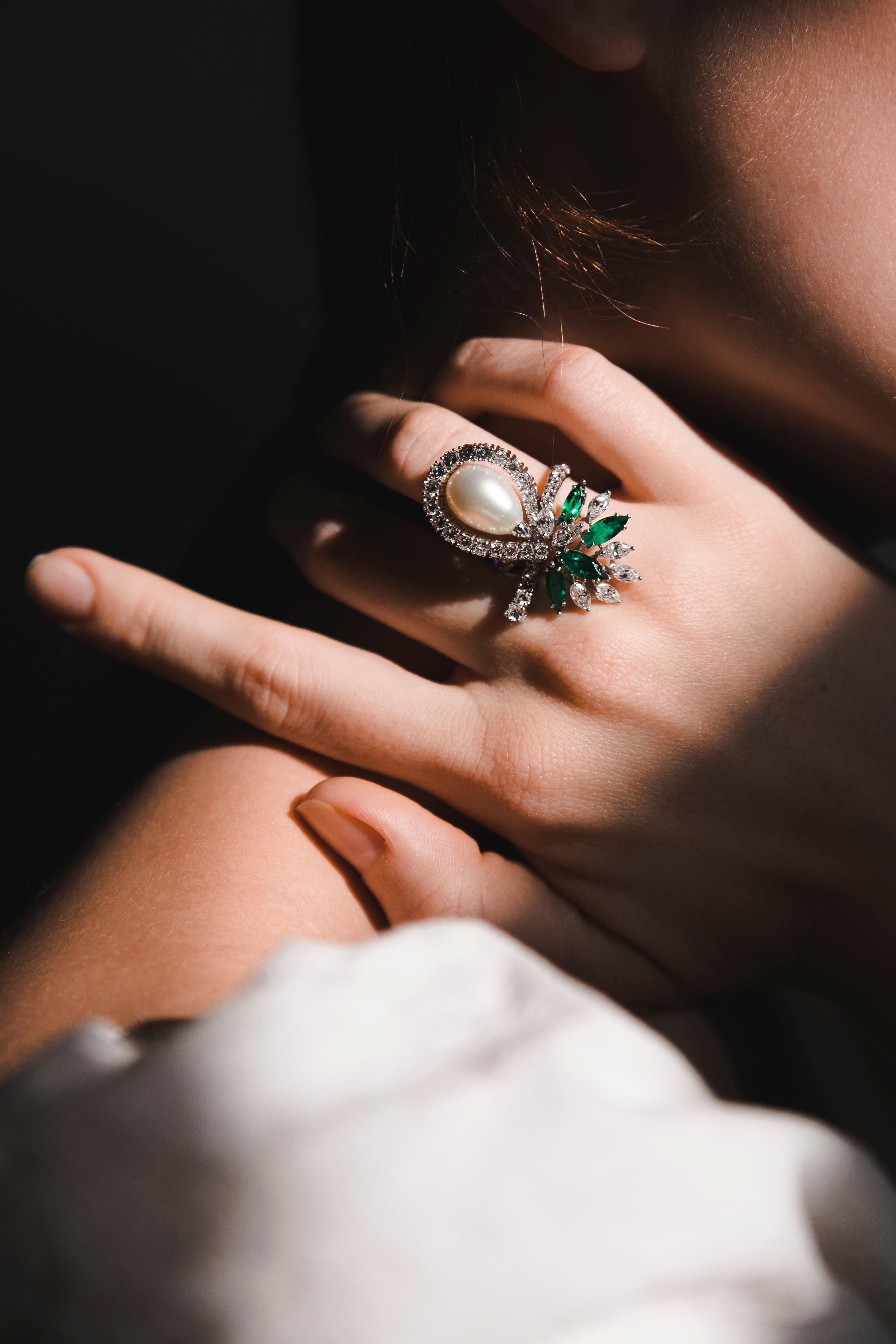 Organic design elements. Fine Emeralds and Diamonds sweep like a ribbon around oval-shaped Pearl. Both Round-cut and Marquise-cut Diamonds are masterfully designed together to create a lightness effect. A bright touch of Colombian Marquise-cut