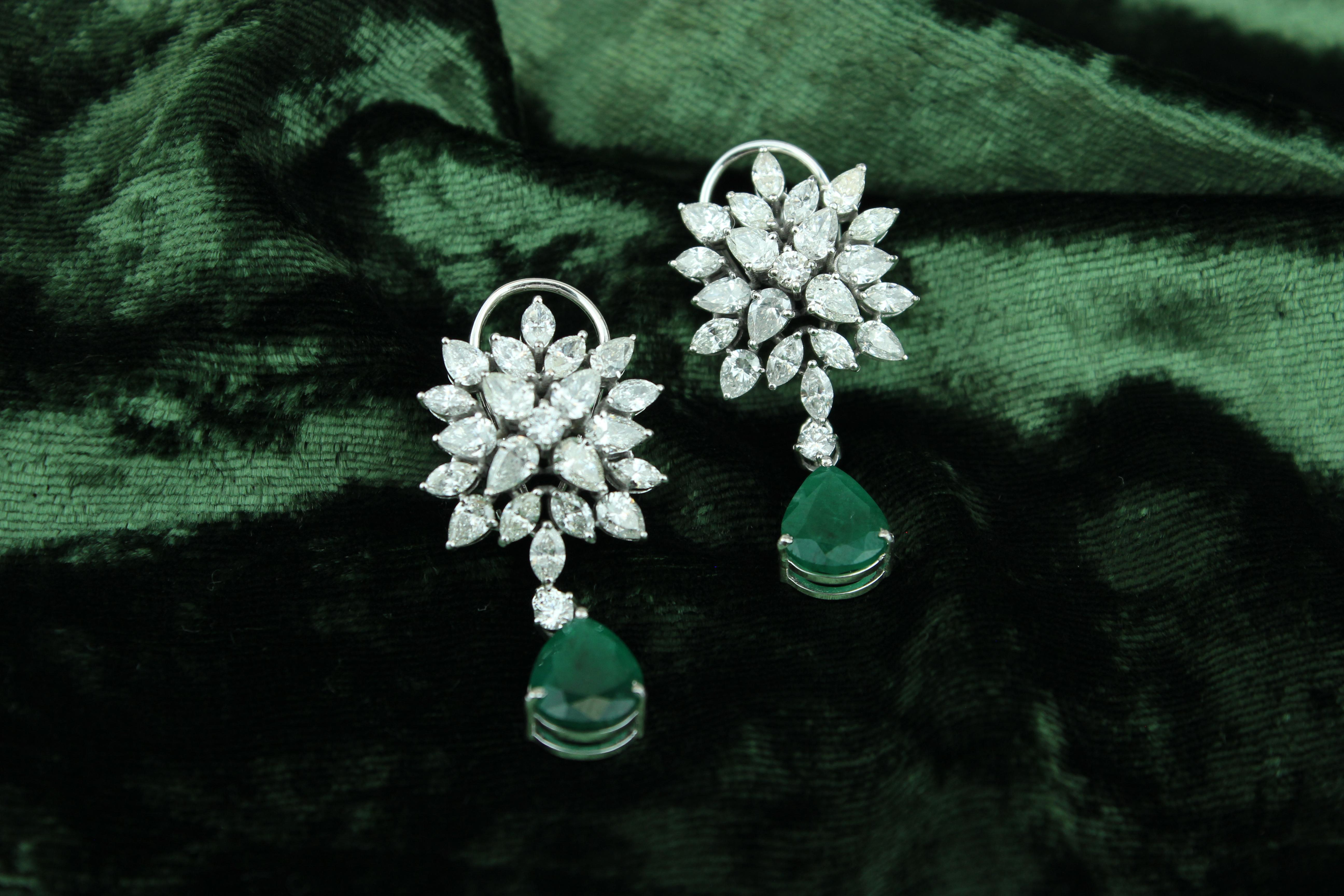 These Earrings are a stunning pair of earrings that showcase the beauty of brilliantly cut marquise and pear shaped diamonds enhanced by emerald gemstones. The earrings feature a unique design with the diamonds arranged in a cluster and set in 18K