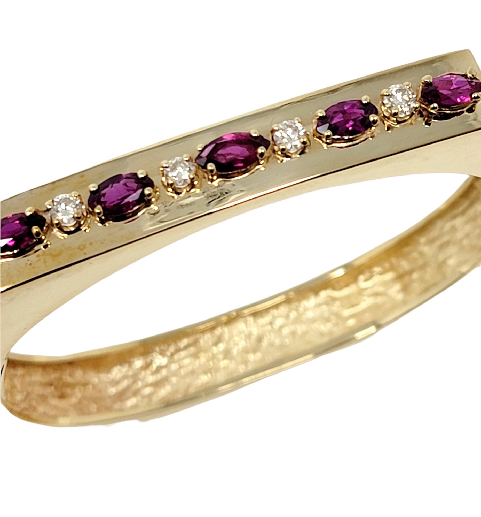 Elegant high polished yellow gold bangle bracelet with sparkling garnet and diamond detailing. The unique geometric design of the bangle gives the piece some added interest, while the colorful rhodolite garnets and shimmering natural diamonds