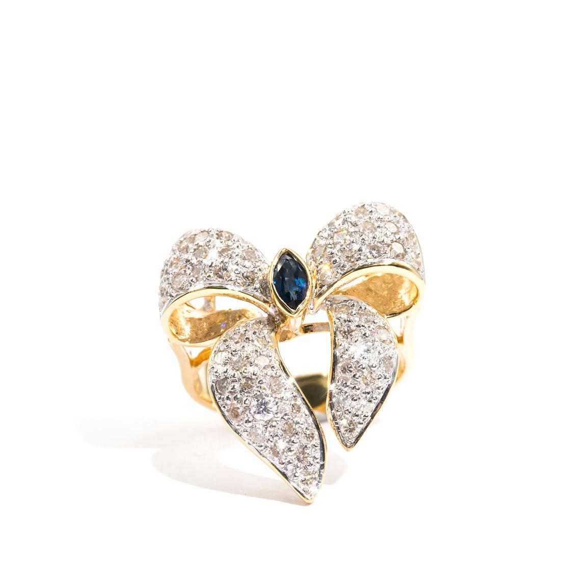 Carefully forged in 18 carat yellow gold is this ever so charming vintage bow cluster ring embellished with 0.80 carats of round brilliant cut diamonds encompassing a marquise natural blue sapphire. We have named this gorgeous vintage splendour The