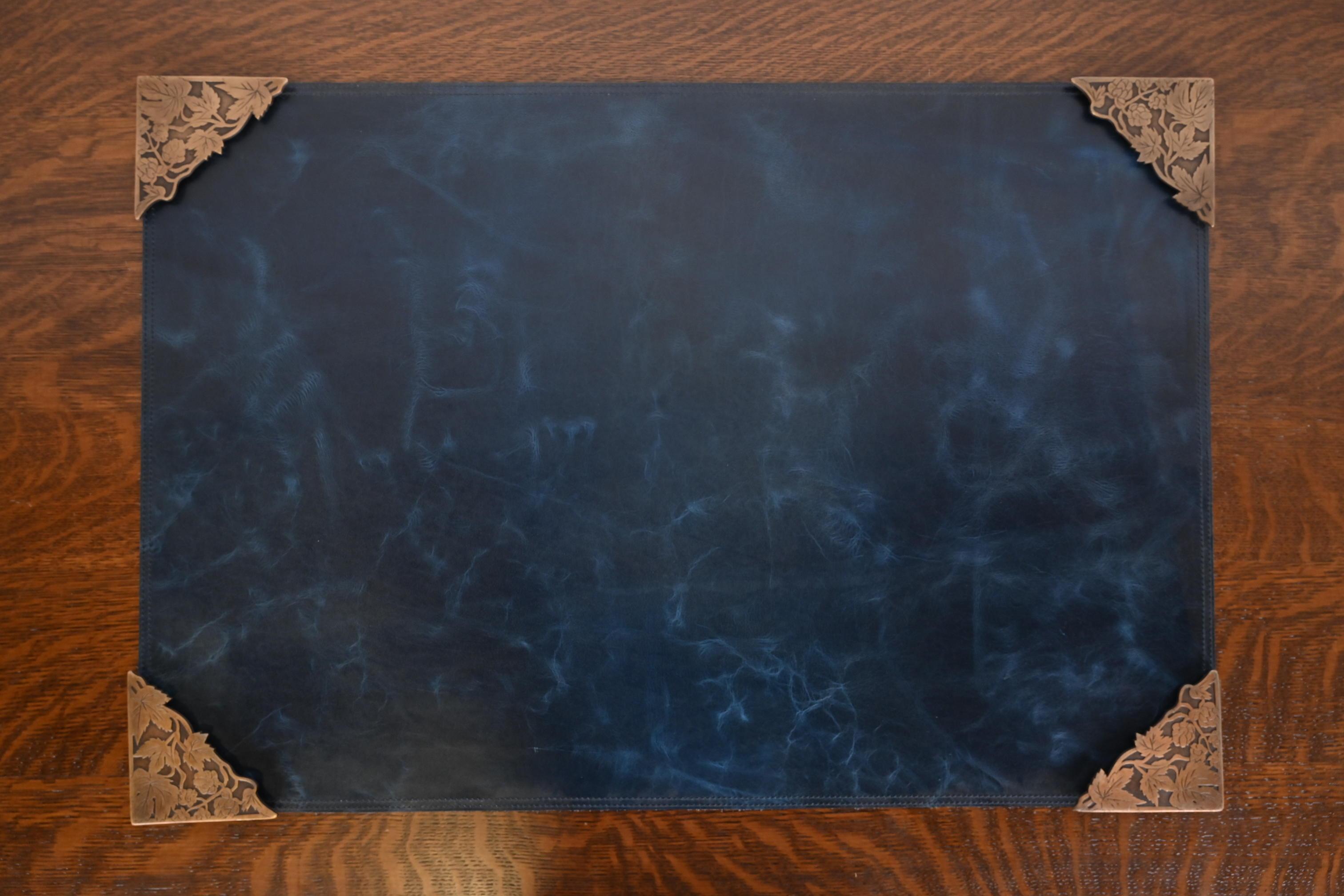 A gorgeous set of four Art Deco or Arts & Crafts period floral ivy bronze blotter corners, with a custom blue leather desk blotter.

In the manner of Tiffany Studios

By Marshall Field & Co. (blotter corners signed to the underside)

USA, Circa