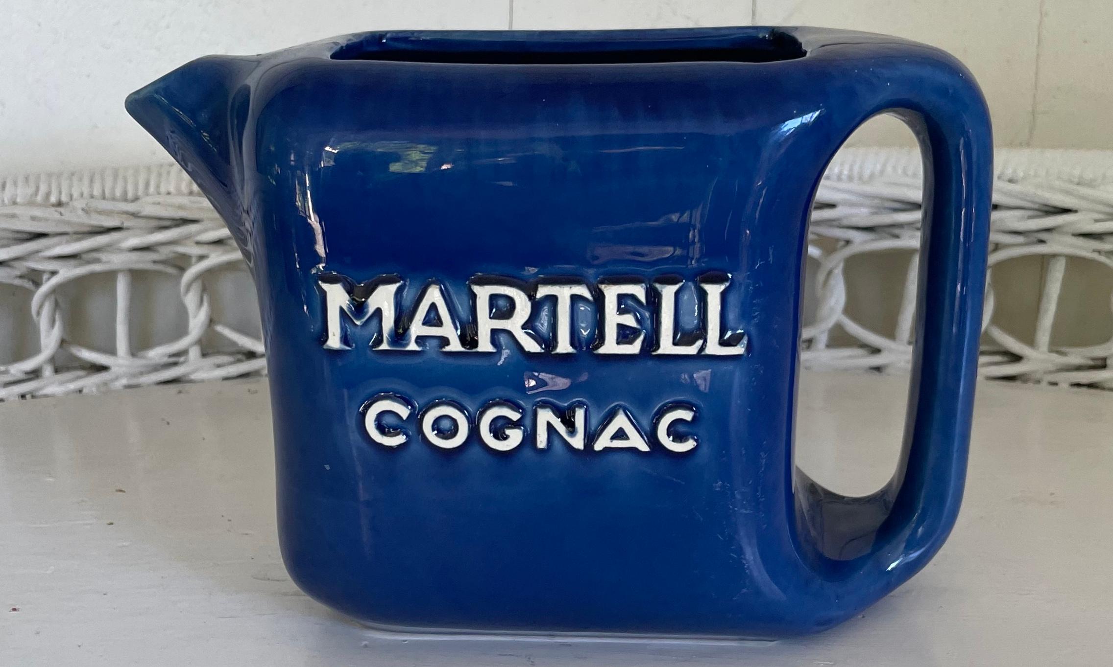 Martell Cognac blue pitcher. Vintage French blue glazed bar water pitcher with the Martell Cognac logo in white with markings for St. Clement factory. France, Mid-20th century. 
Dimensions: 8” W x 3.75