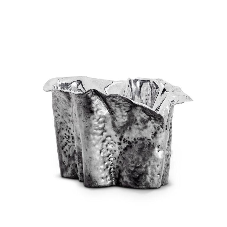 The Martellato Elevated Champagne Cooler redefines elegance through a seamless union of artistry and functionality. Crafted in polished metal with a silver finish, it stands as both a sculptural centerpiece and a practical serving piece. Its fluid,