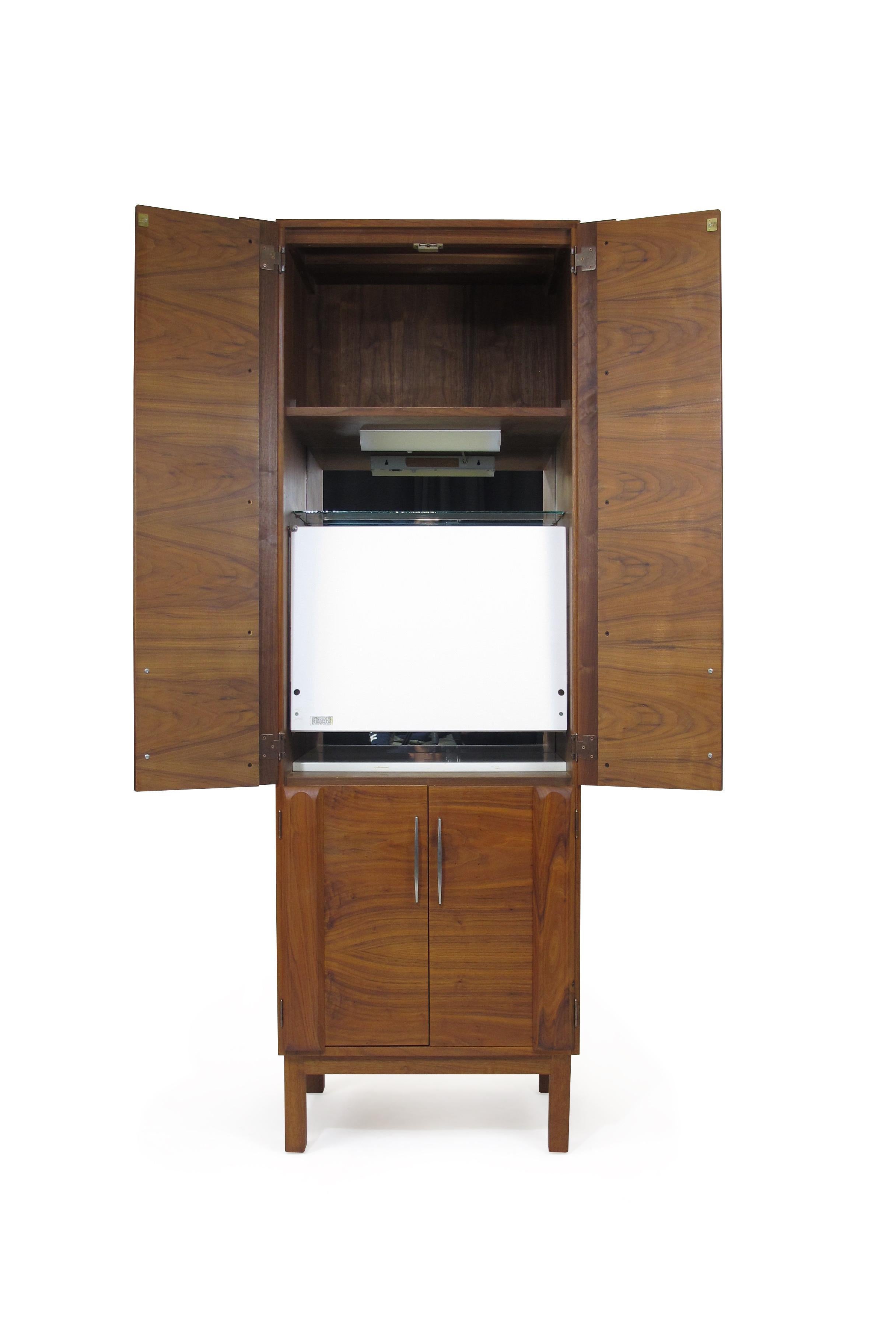 Tall and narrow midcentury walnut bar cabinet designed by California architect Martin Borenstein for MB design, circa 1960, US. Crafted of walnut wood and features four doors with aluminum pulls which enclose: a flip open mirrored bar, two glass