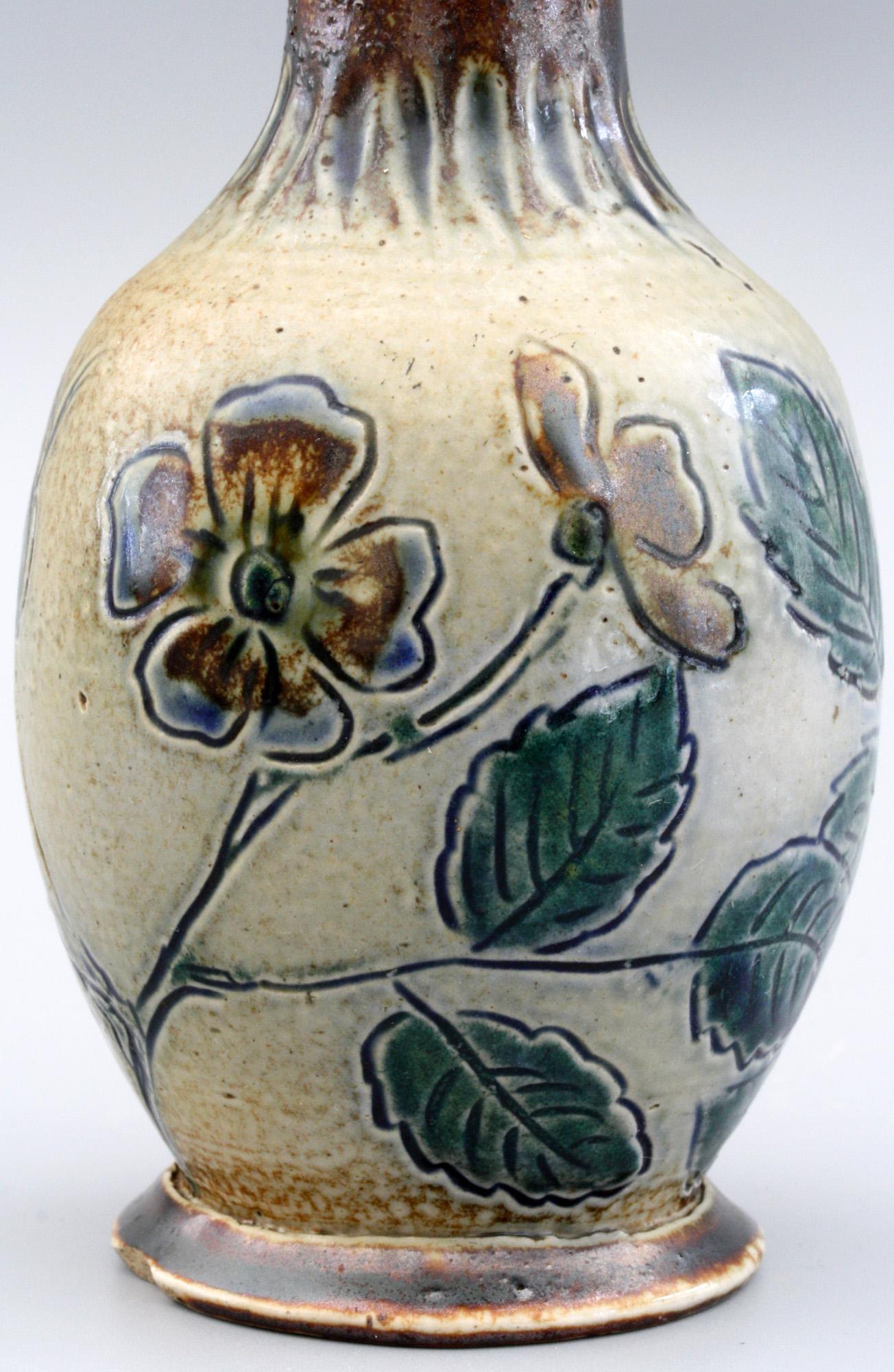 A Martin Brothers stoneware art pottery vase decorated with incised flowering dog roses decorated in brown and blue glazes dating from the 19th century. The small bottle shaped vase stands on a wide rounded foot with a rounded bulbous body and a