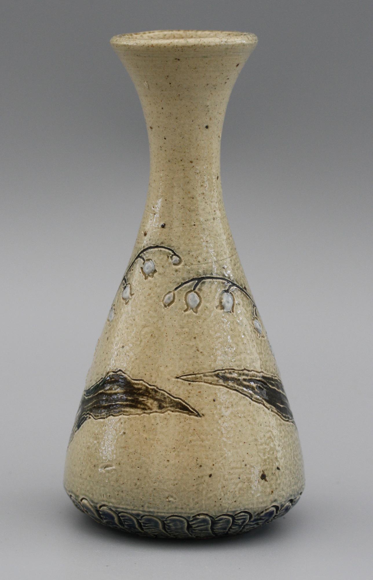A Martin Brothers stoneware art pottery vase decorated with Lilies of the Valley and decorated in brown, blue and white glazes dating from the latter 19th century. The conical flask shaped bottle vase stands on a wide rounded foot with a patterned