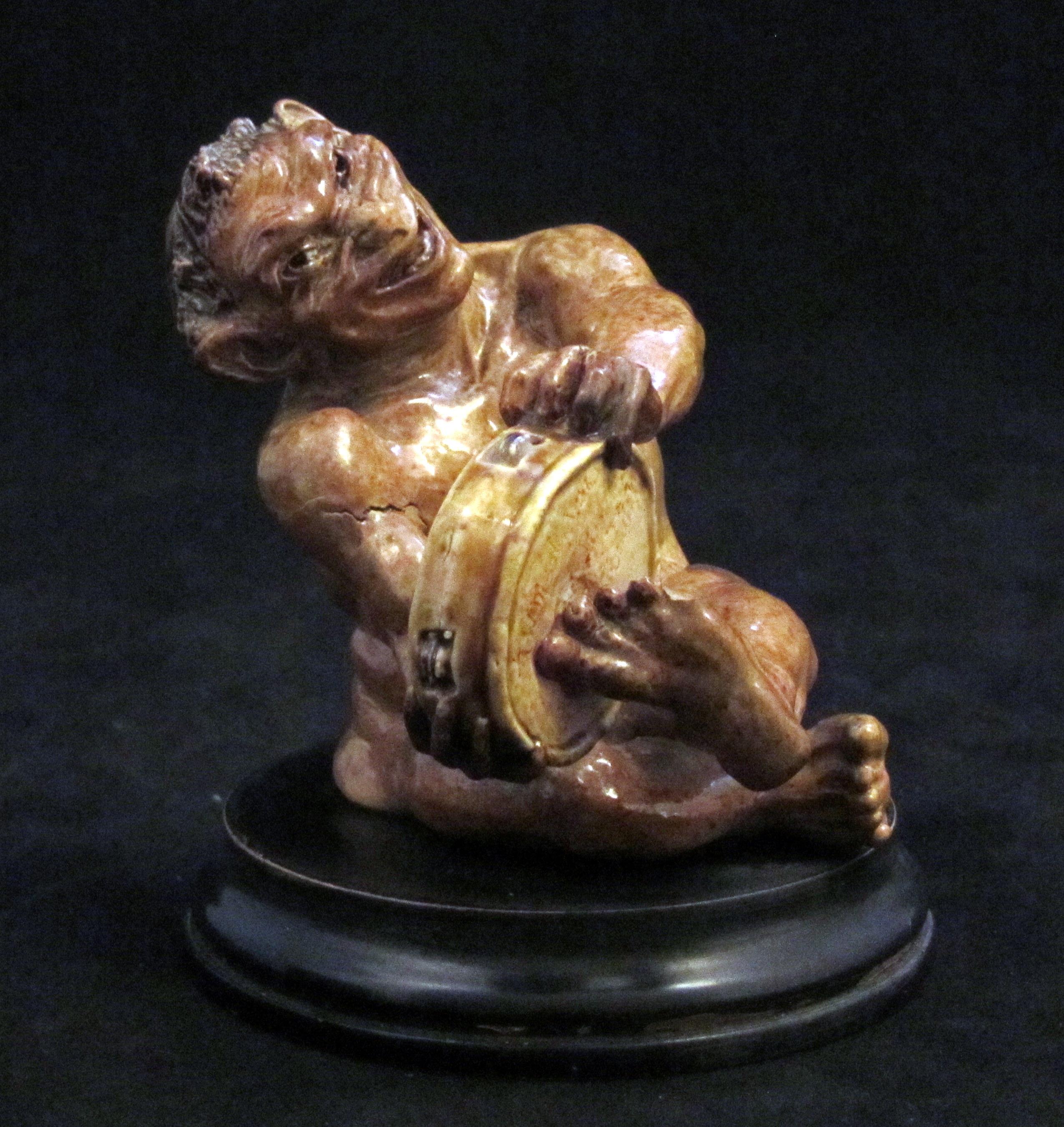 4697
Martin Brothers Characterful Musical Imp.
Seated figure on am ebonised stand playing the Tambourine.
Toe to left foot missing.
Signed to the Tambourine
Circa 1895.