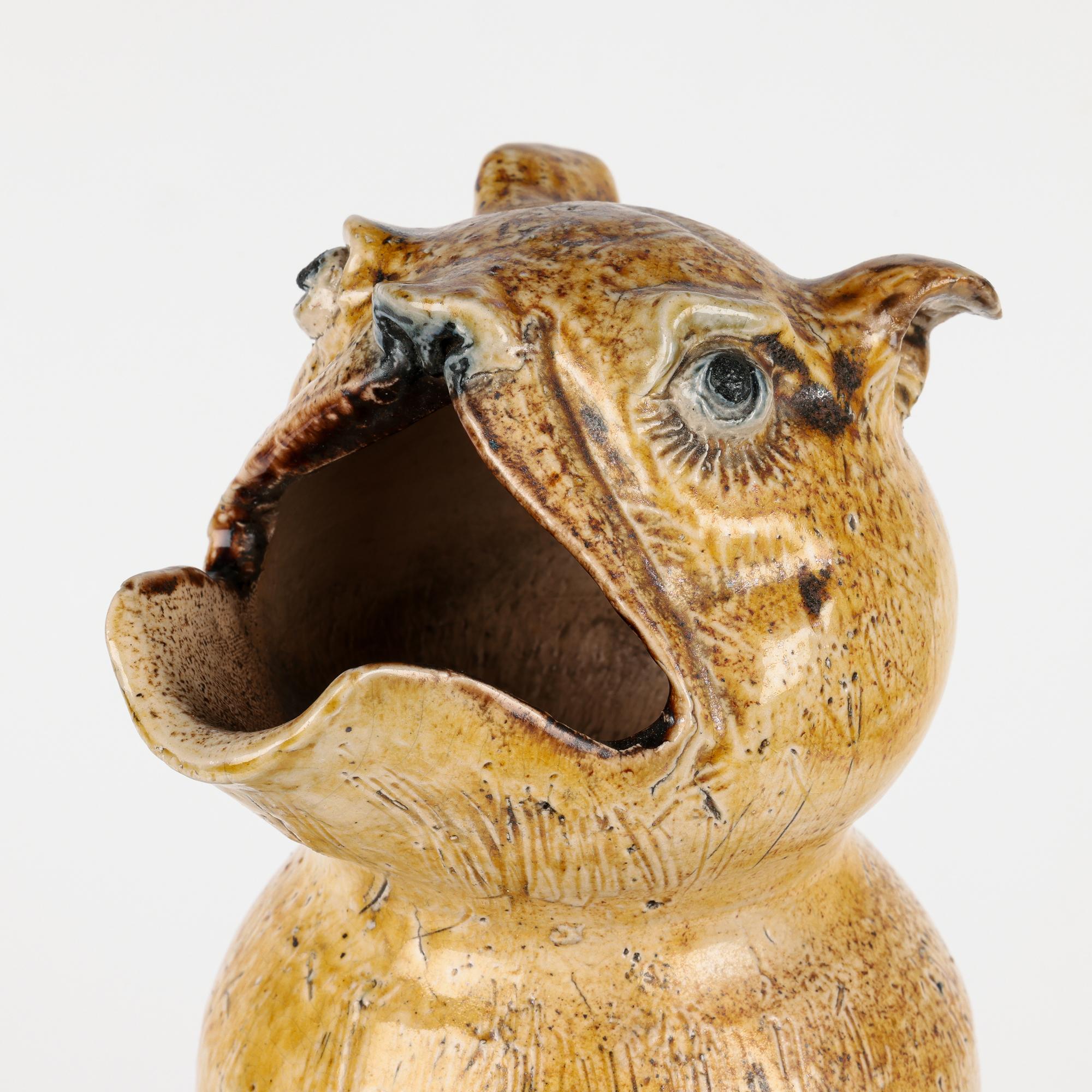 An extremely rare and probably unique, tall grotesque figural ewer or spoon/ladle warmer by Robert Wallace Martin for the Martin Brothers dated 1880. The stoneware ewer is of tall cylindrical shape and is modelled as a fanciful animal seated upright