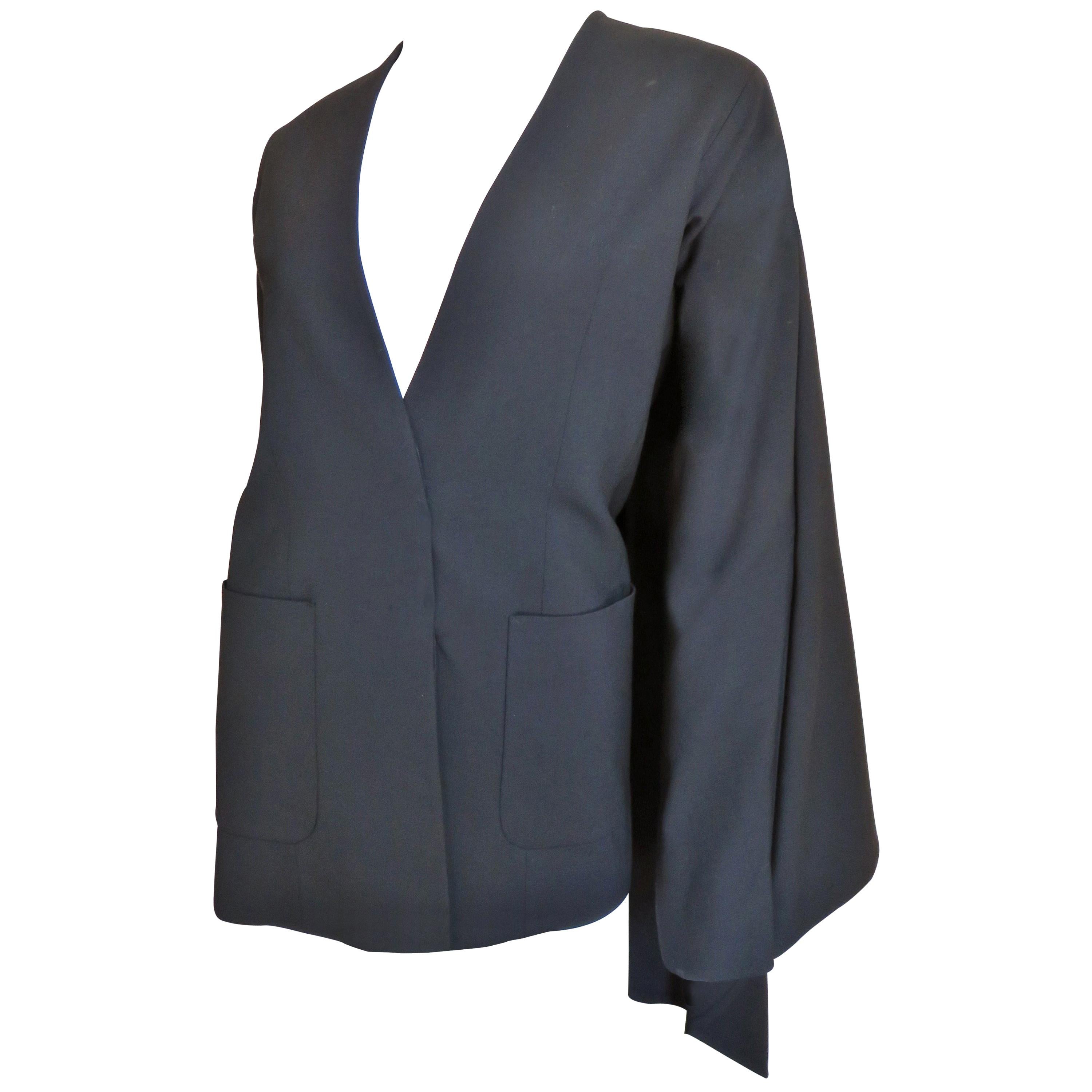 A fabulous dramatic black fine wool jacket from Martin Margiela.   It is collarless with long sleeves, a hidden button front closing and 2 front patch pockets.  The back is stunning with a back cape draping from the shoulders and back of the