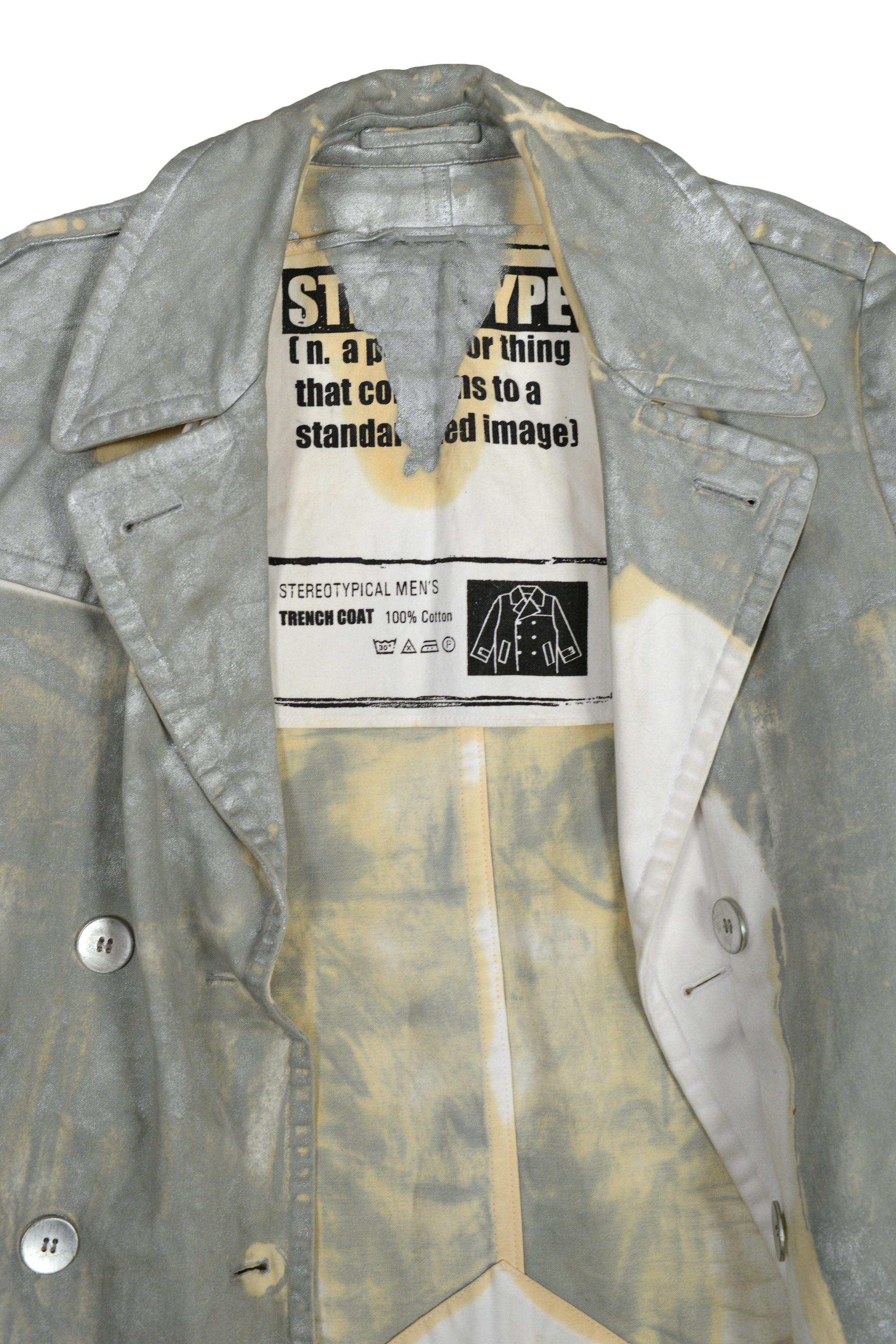 Resurrection Vintage is excited to present a vintage Maison Martin Margiela white canvas double-breasted trench coat featuring all-over silver paint, a matching waist belt, back vent, and classic trench coat details.  There is a broken button on the