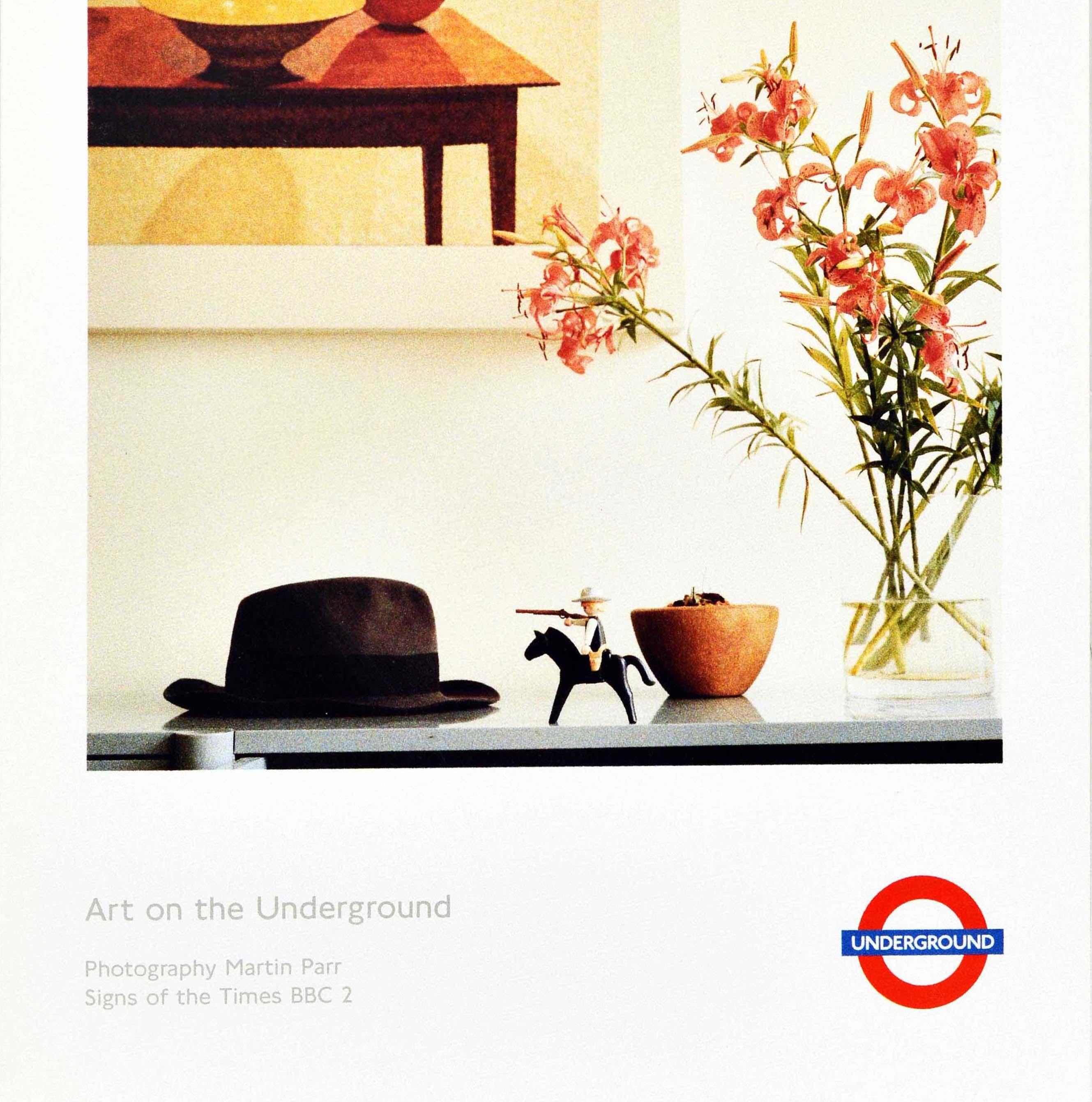 Original vintage London Underground poster featuring a side table with a hat and flowers in a vase on it, a framed artwork on the wall and a child's toy horse with the rider holding a gun to the hat in front of a decorative bowl, the caption above