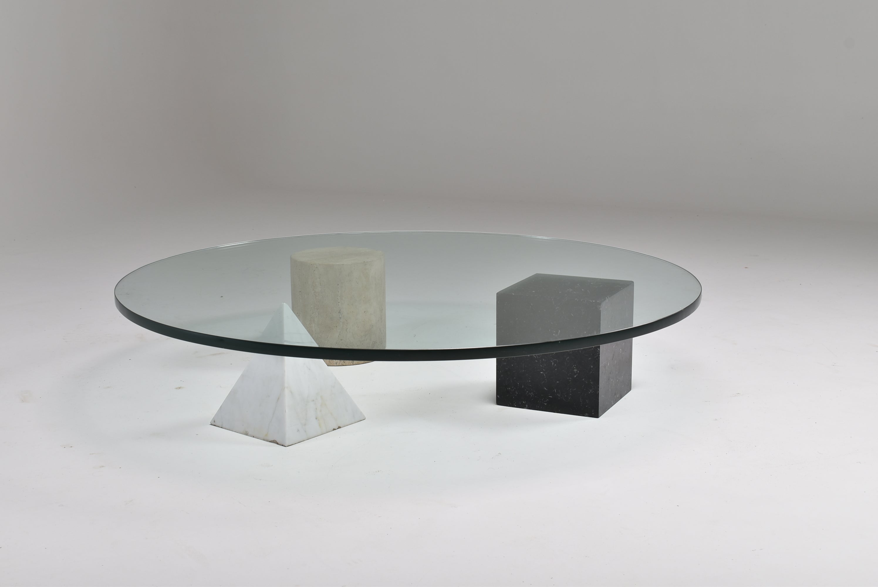 Forms of the Euclidean geometry, the cube, the cylinder, and the pyramid, made of three different marbles and colours, represent the basis of the table finished with a big sheet of transparent glass. The three elements are independent and can be