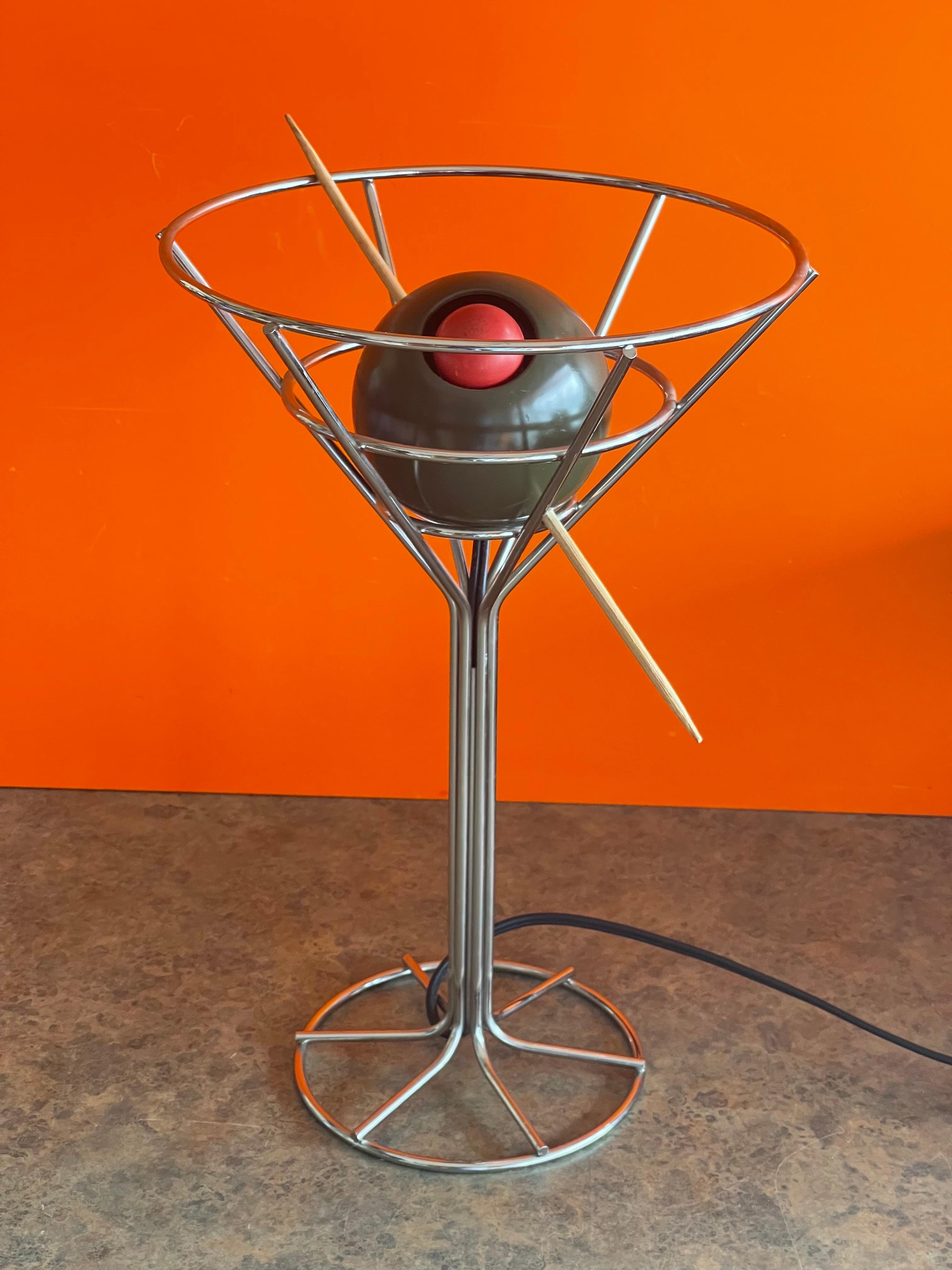 A unique and hard to find vintage martini with olive bar lamp by David Krys, circa 1993. The pop art lamp is made of chrome and molded plastic and has a pimento red bulb with toothpick; this piece is extremely cool! The lamp is in good working
